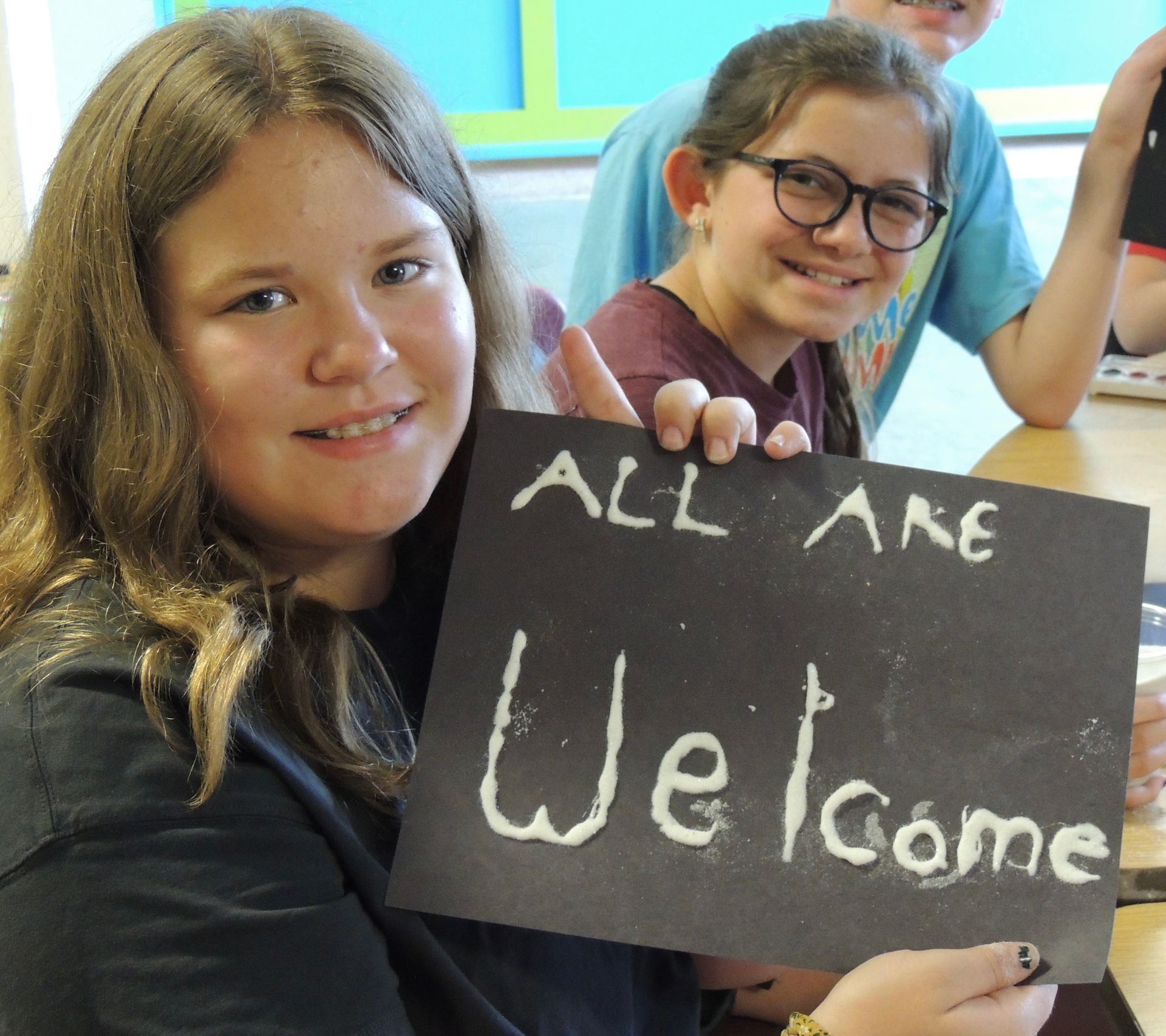 Children smile and hold a sign reading