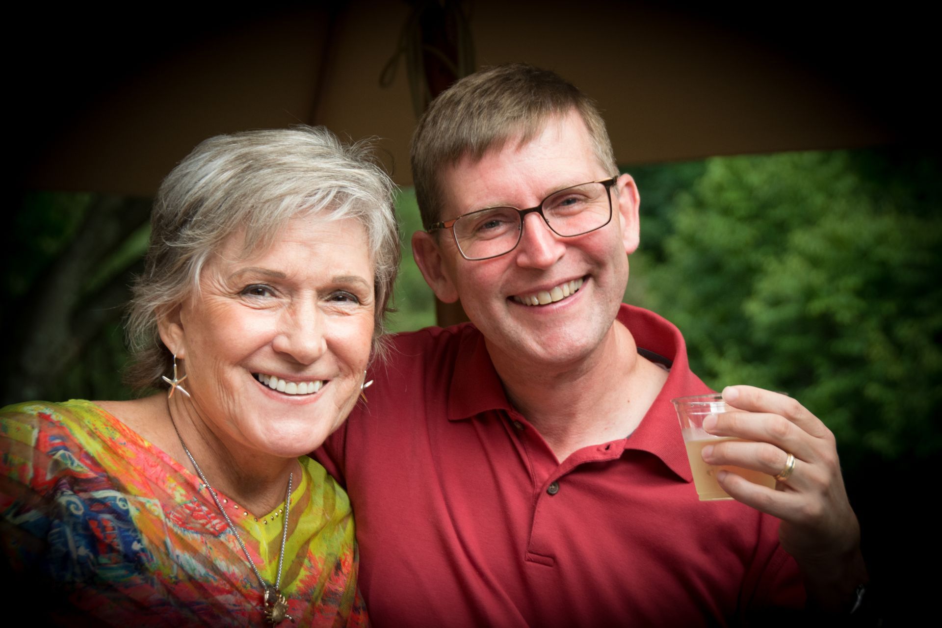 A woman smiles as a man to her right smiles holding a drink