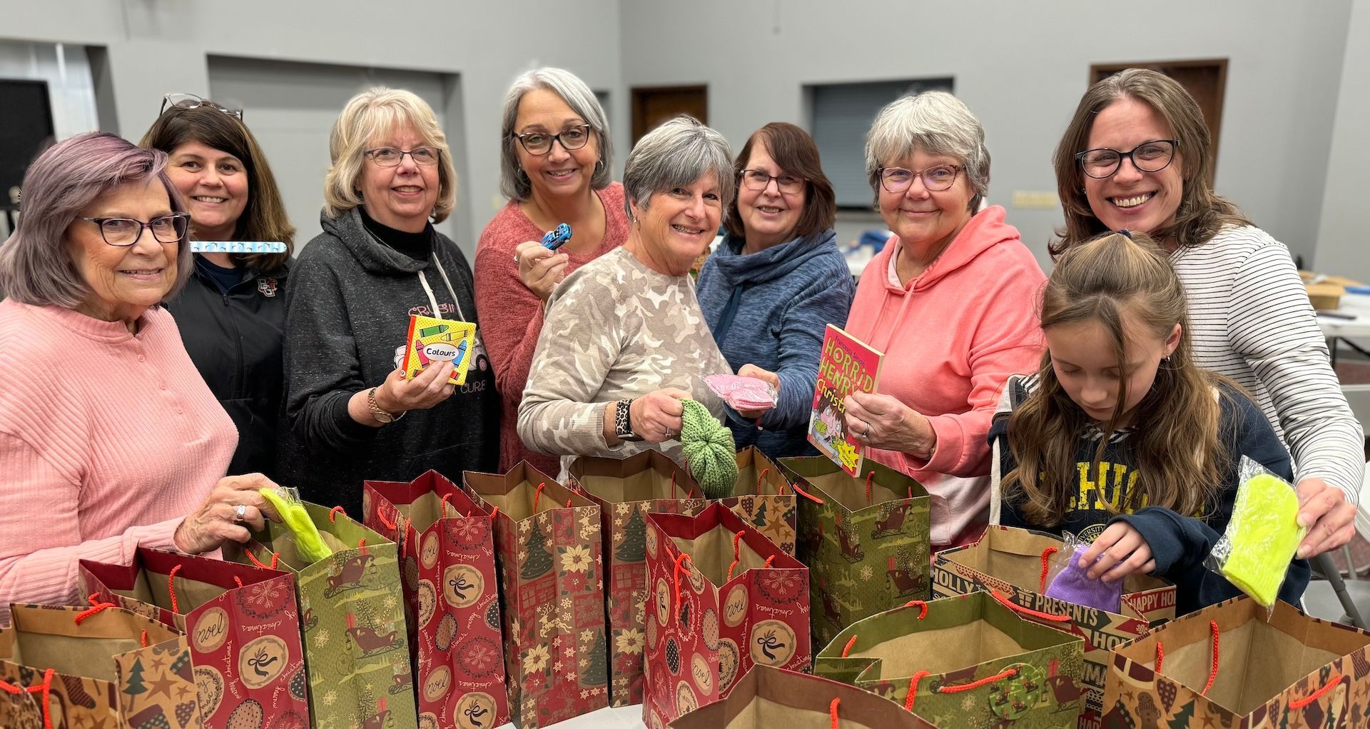 A group of women smile behind gift bags on a table