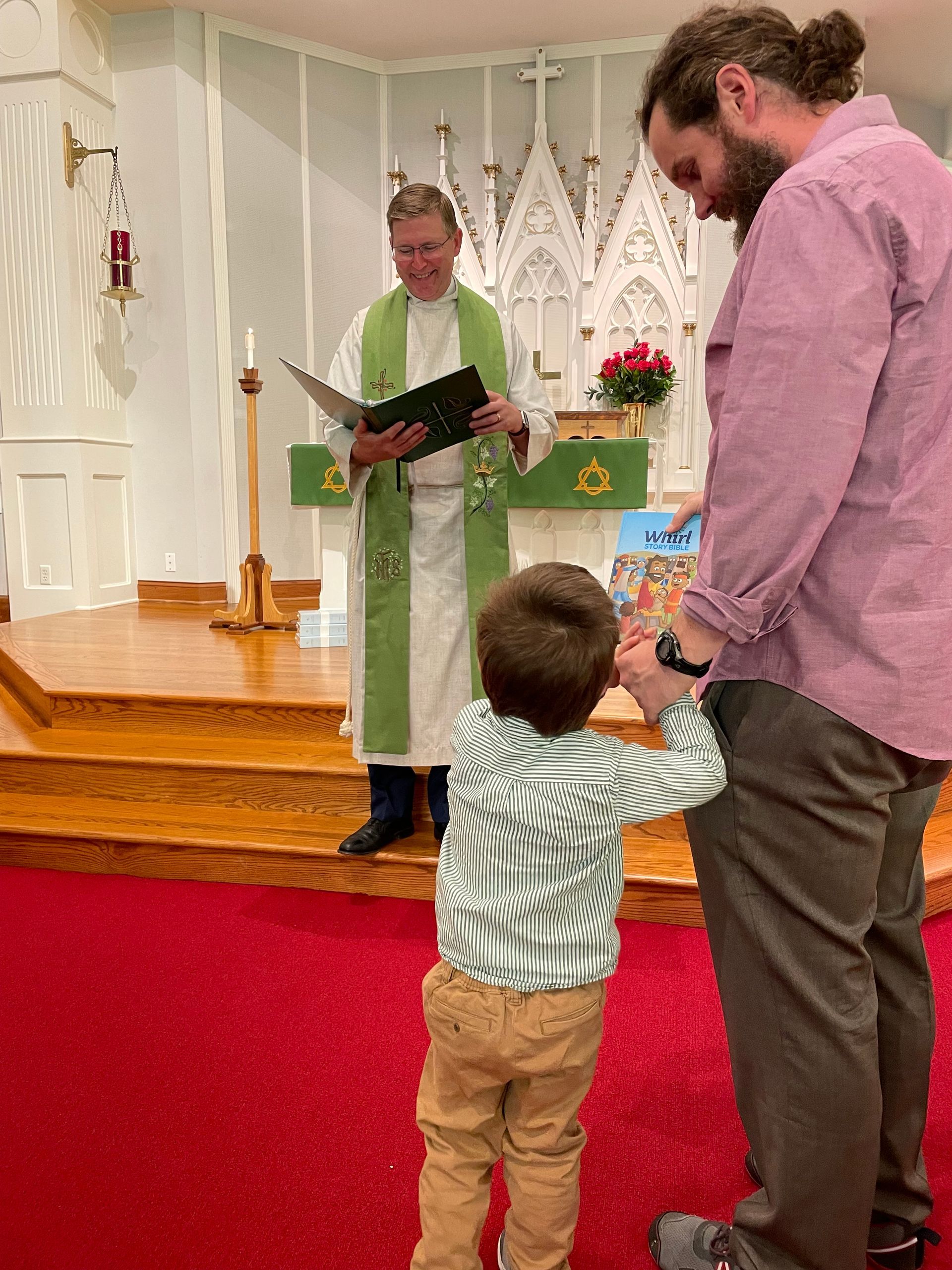 A pastor reads prayers from a book, a man to his right bows his head