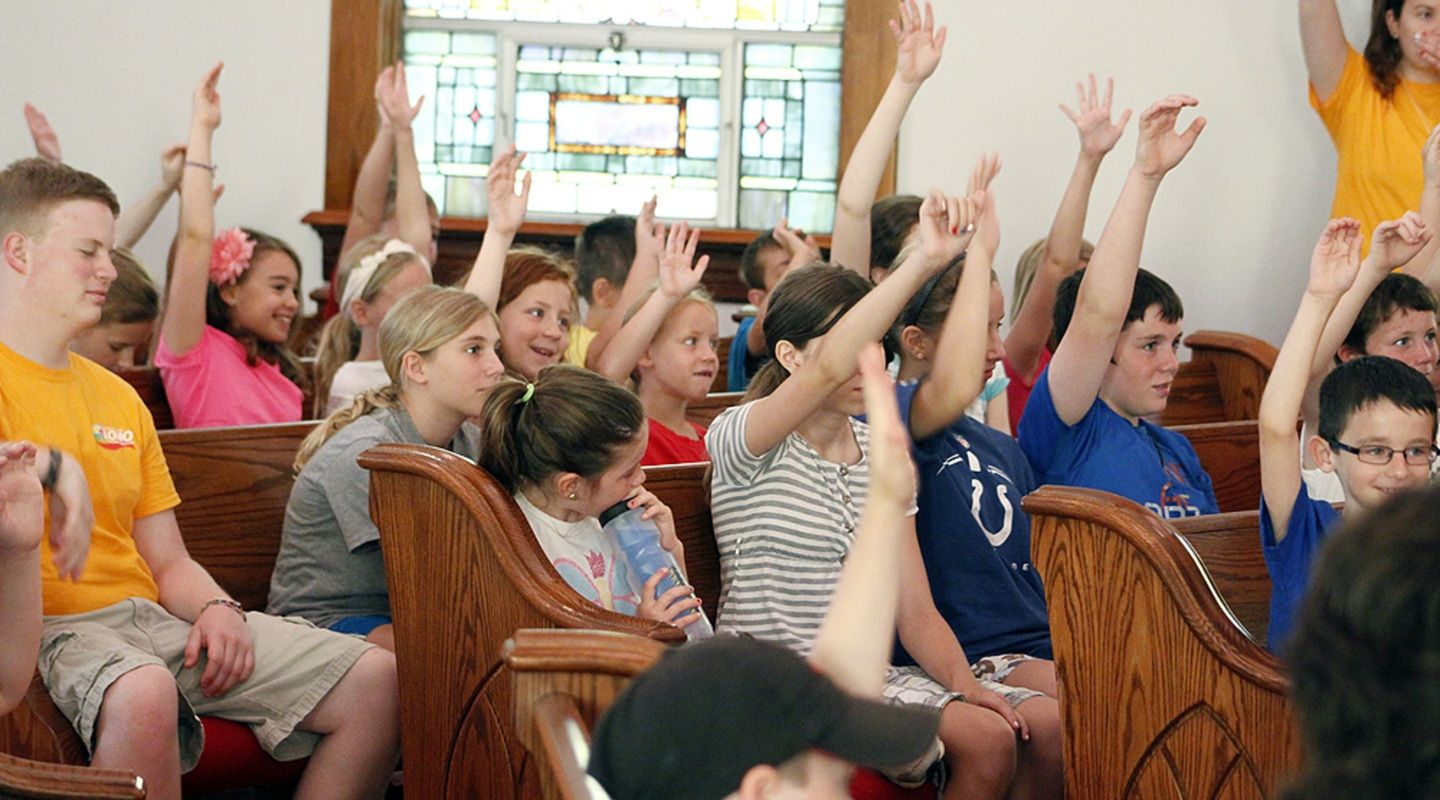 A group of children raise their hands to ask questions in a church sanctuary