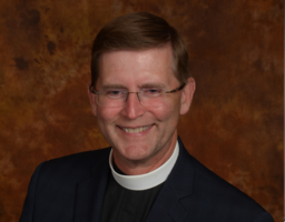 Pastor Jonathan Bull smiles in front of a brown background