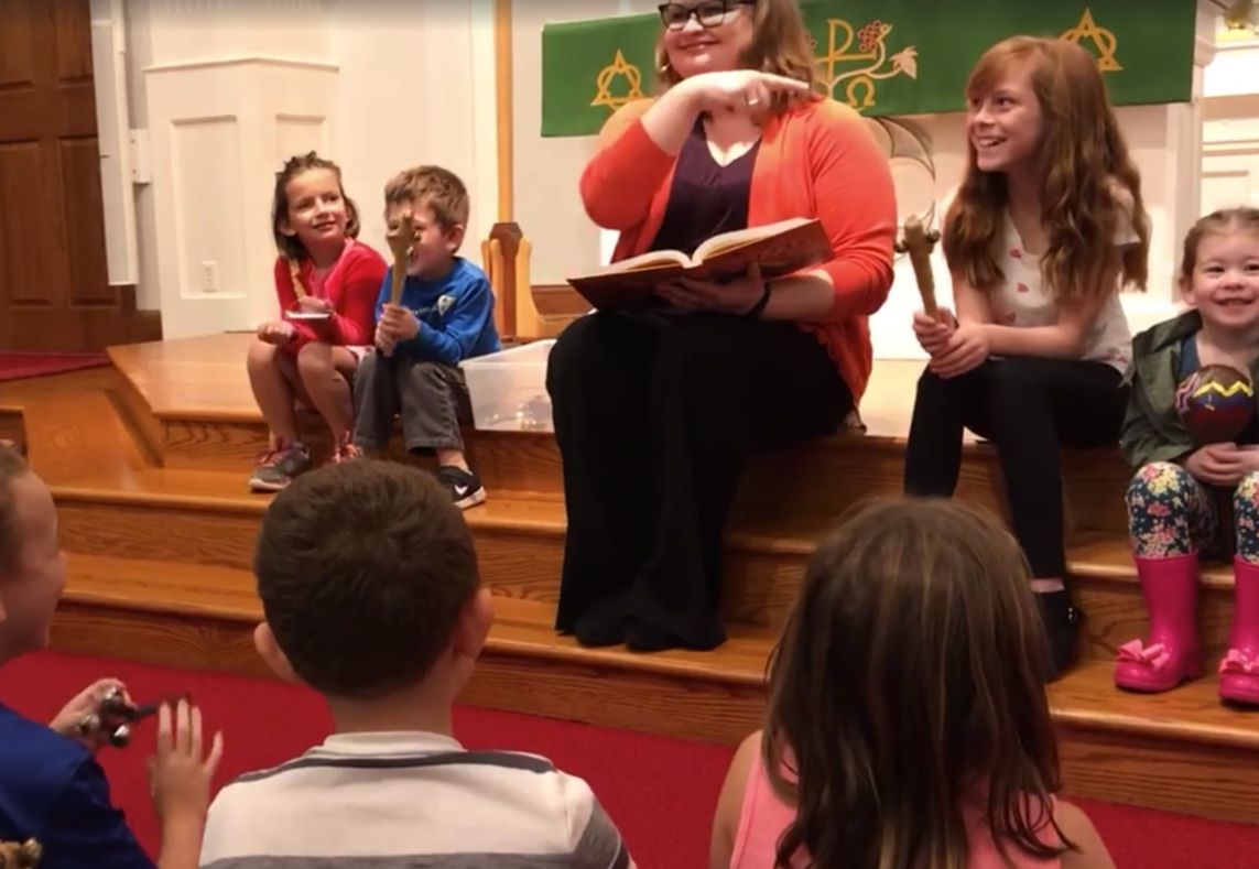 A pastor reads a book to kids at the front of a church sanctuary
