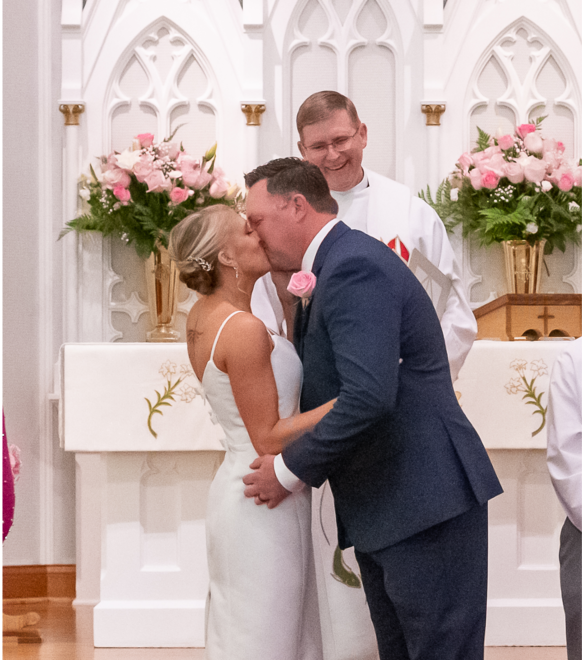 A bride and a groom share their first kiss in front of a pastor