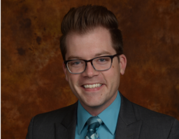 Zach Ruppel smiles in front of a brown background