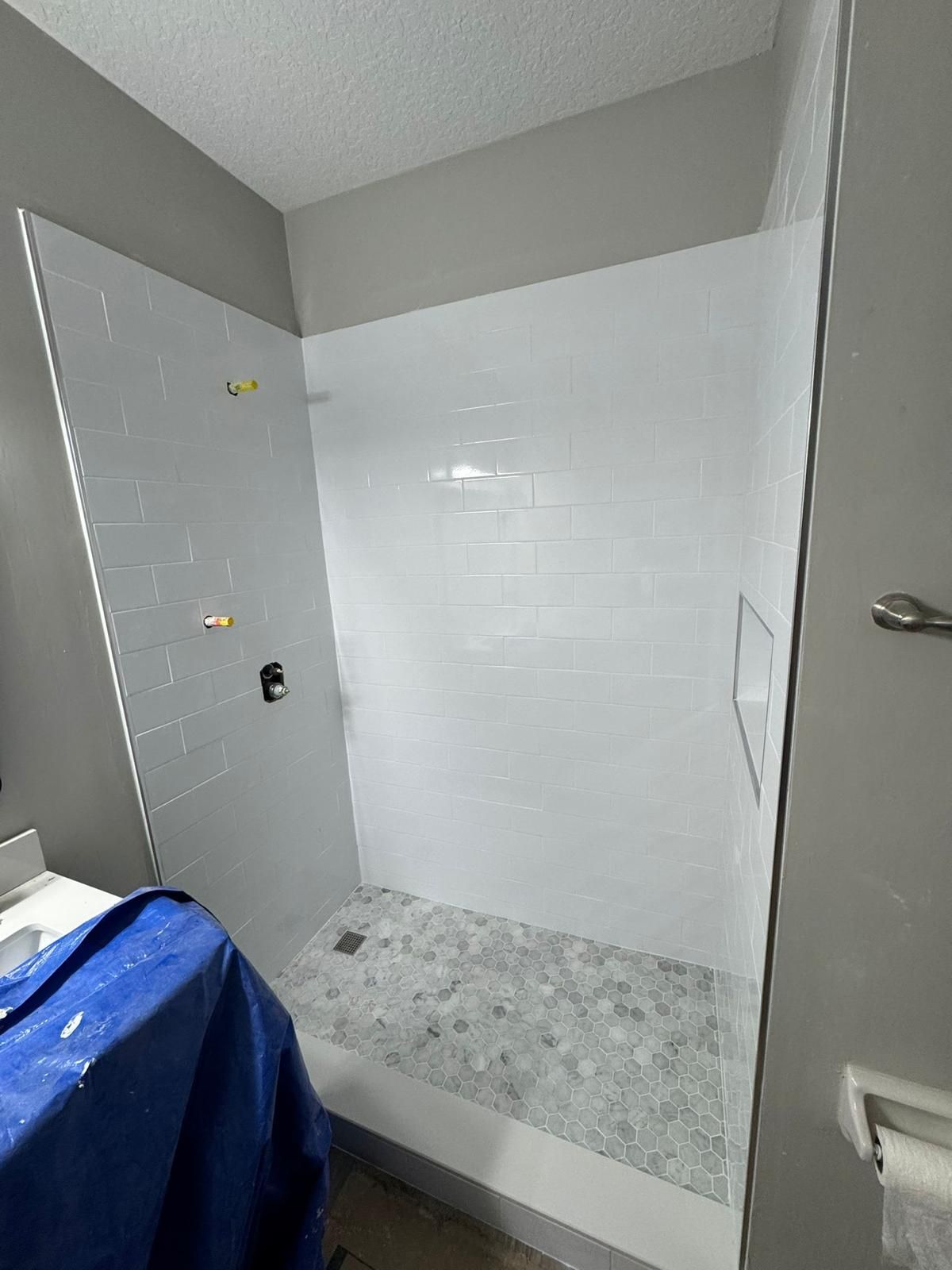 Small bathroom shower area with white tile walls and a blue tarp-covered item on the left