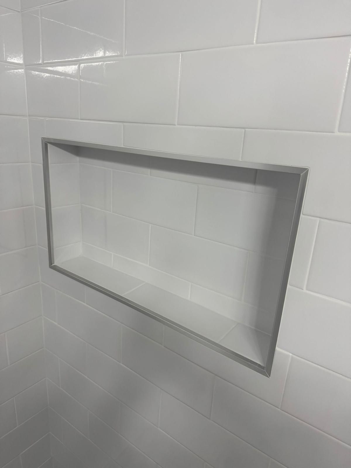 Rectangular recessed niche in a white tiled shower wall with a gray border