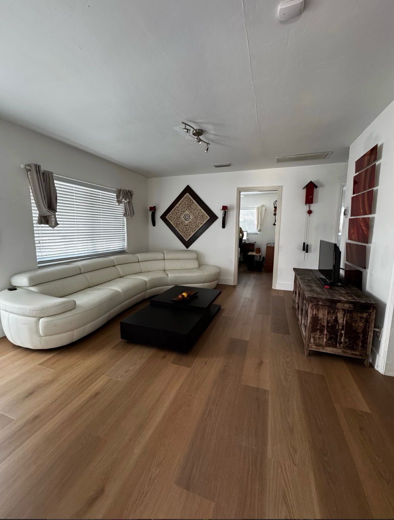 Modern living room with white sectional sofa, black ottoman, wood floors, and a decorative wall mirror