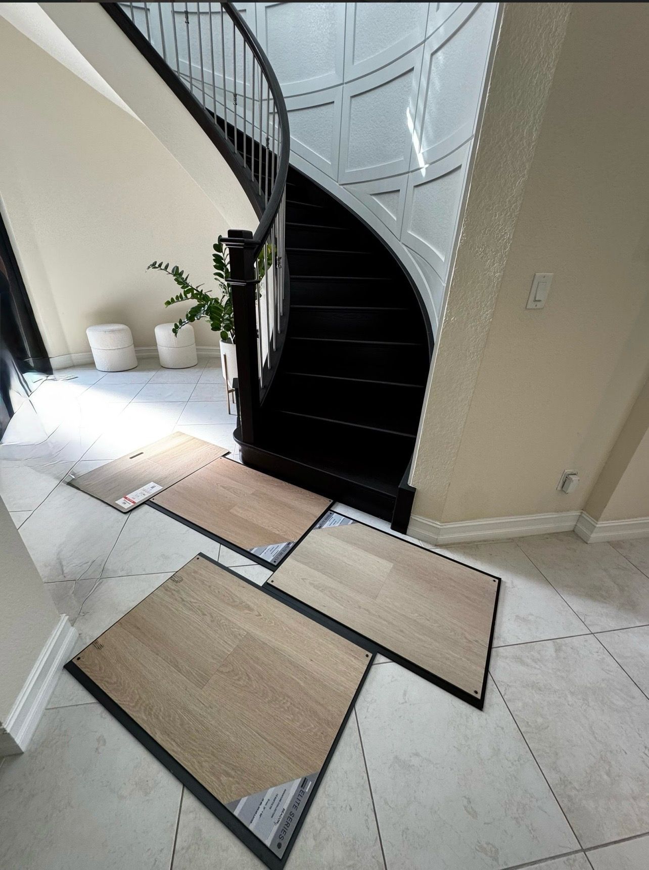Stairwell landing with black curved stairs and cardboard sheets laid over a tiled floor as a temporary walkway