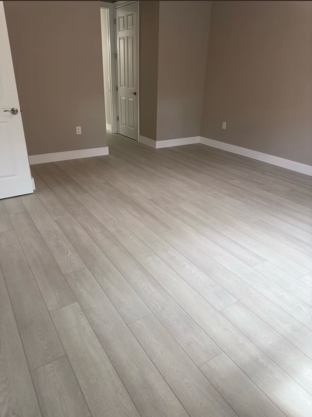 Empty beige room with light wood flooring, white trim, and an open doorway.