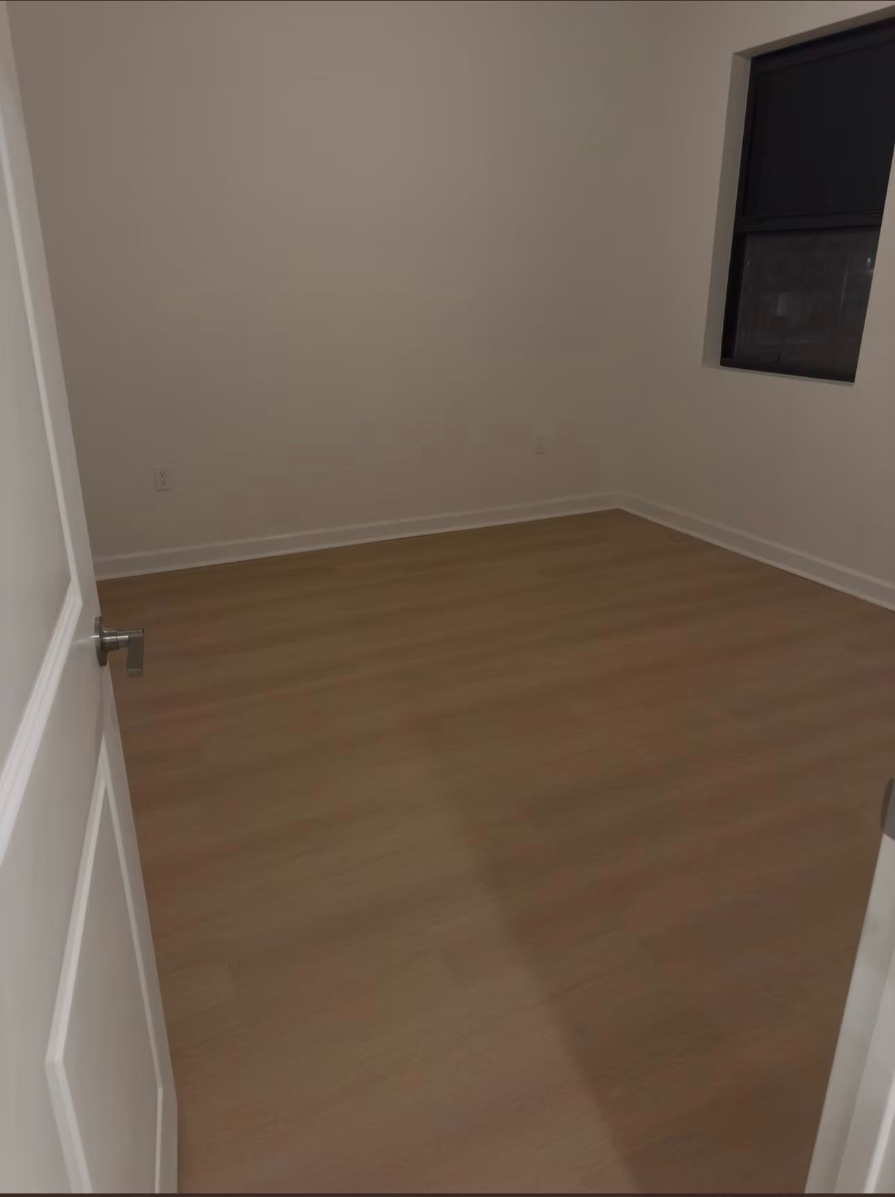 Empty beige room with wood floor and a single dark window.
