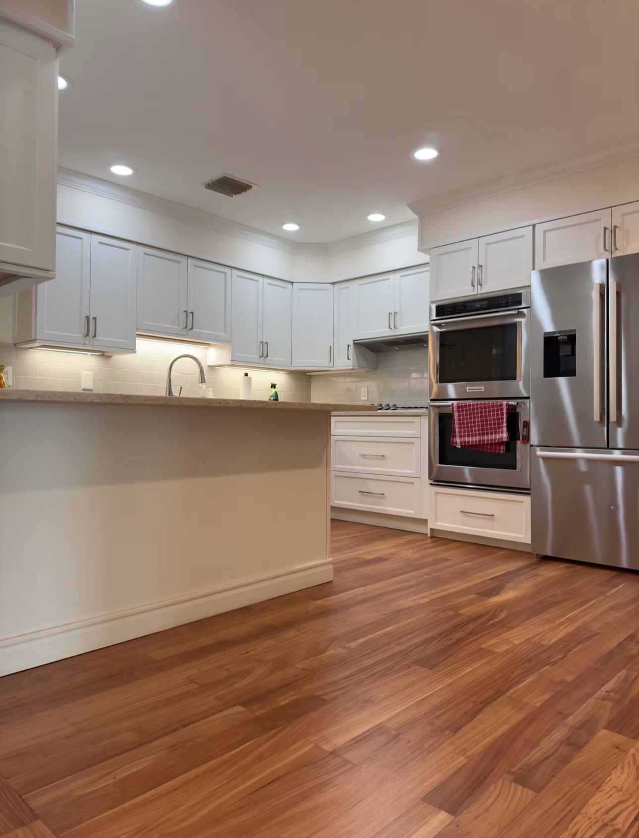 Bright modern kitchen with white cabinets, stainless steel appliances, and hardwood floors