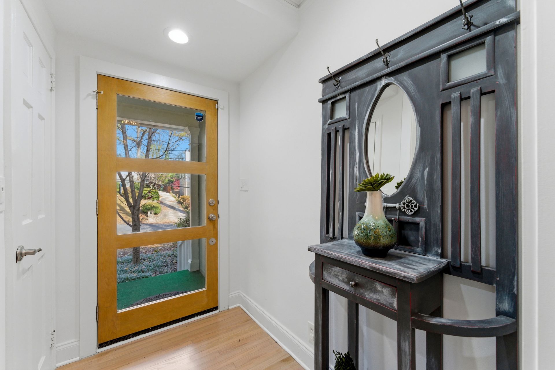 An entryway with a wooden-framed front door and a dark wood hall tree with a mirror and small decorative table.