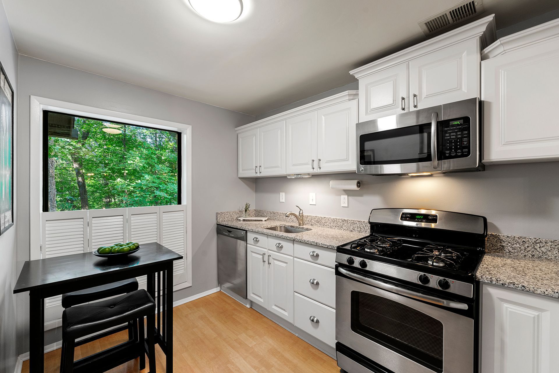 A kitchen with white cabinets , stainless steel appliances , a table and chairs.