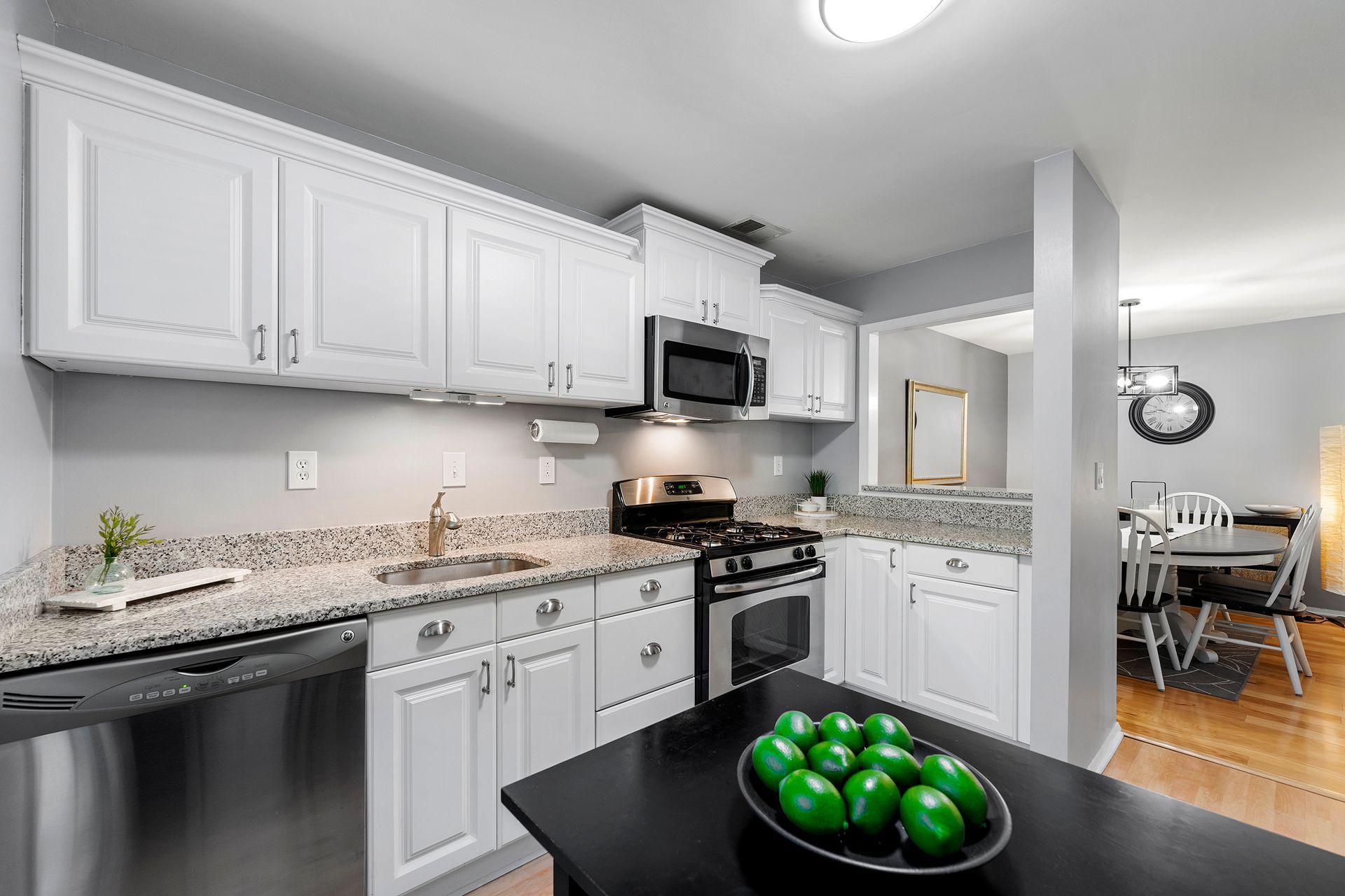 A kitchen with white cabinets and stainless steel appliances and a bowl of green apples on the counter.