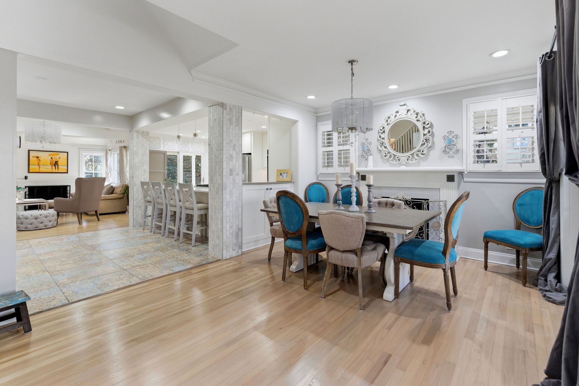 A dining area with a wood table, turquoise and beige chairs, and a chandelier, opening to a bright living room.