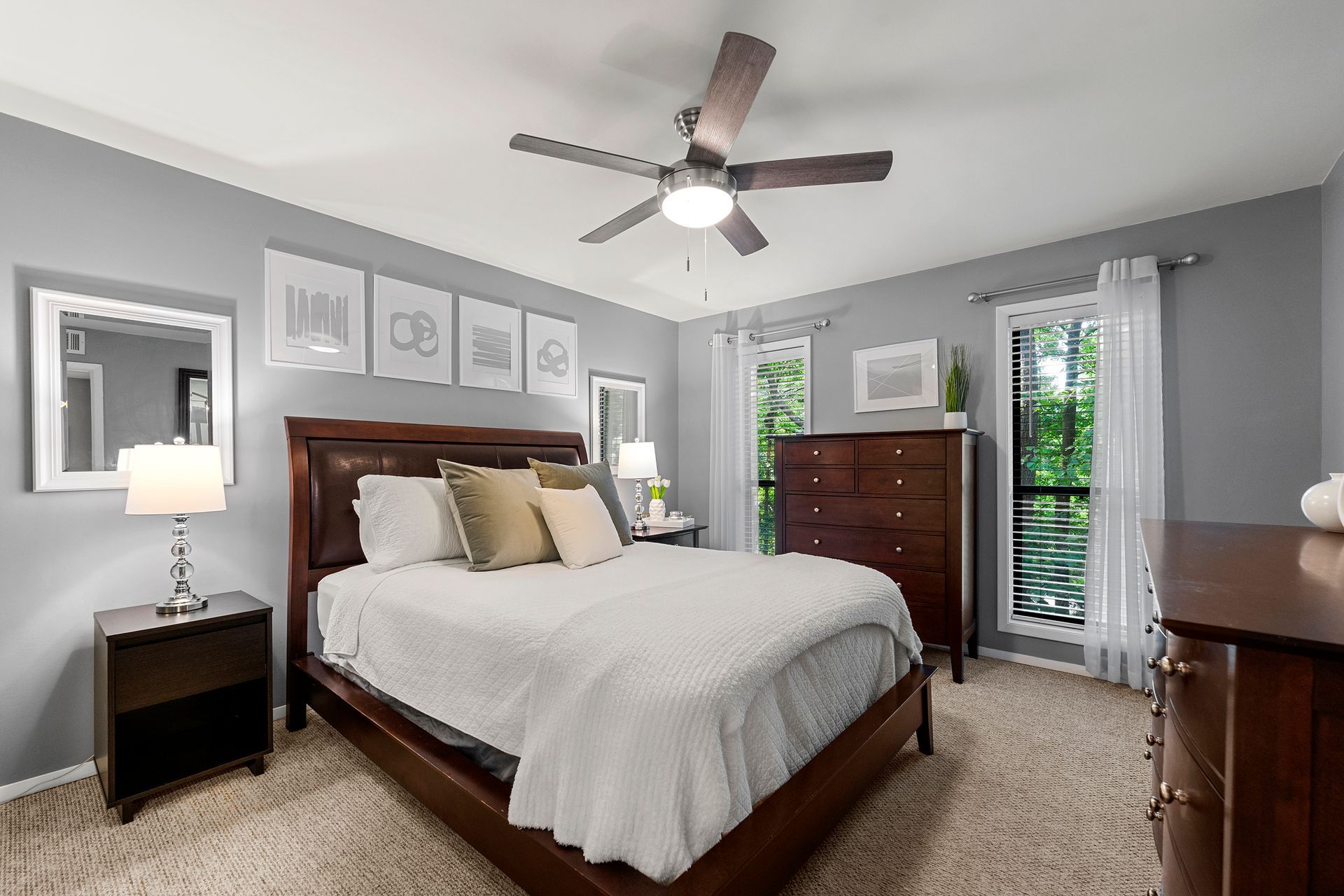 A bedroom with a bed , dresser , nightstand , mirror and ceiling fan.