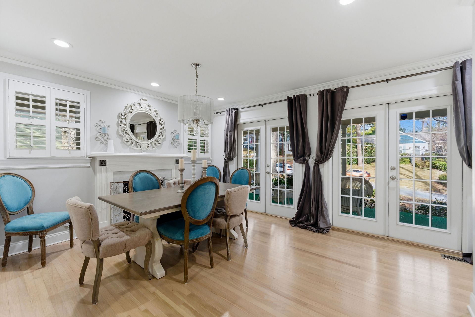 A bright dining room with a wooden table, blue upholstered chairs, a fireplace, and glass doors with dark curtains.