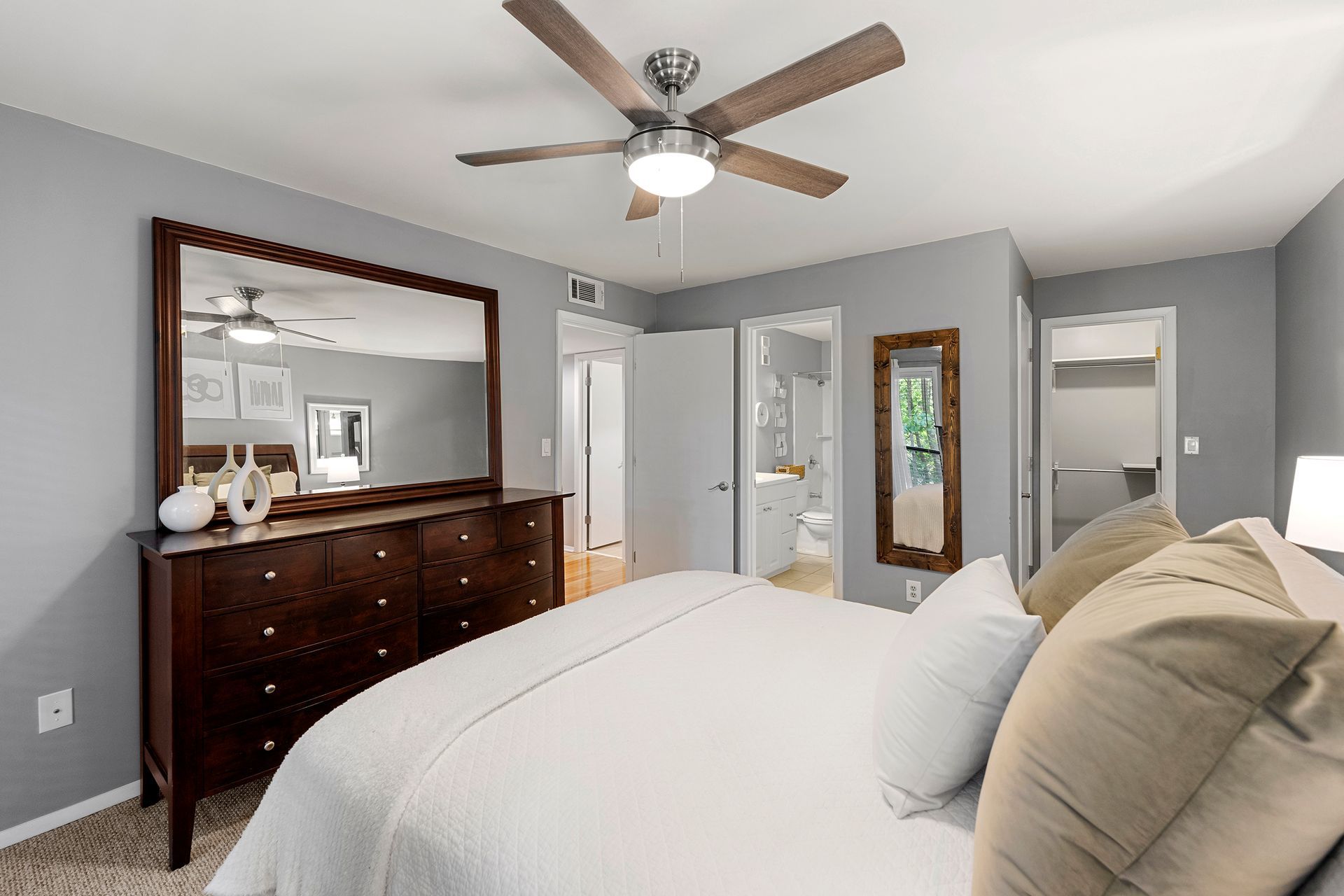 A bedroom with a bed , dresser , mirror and ceiling fan.