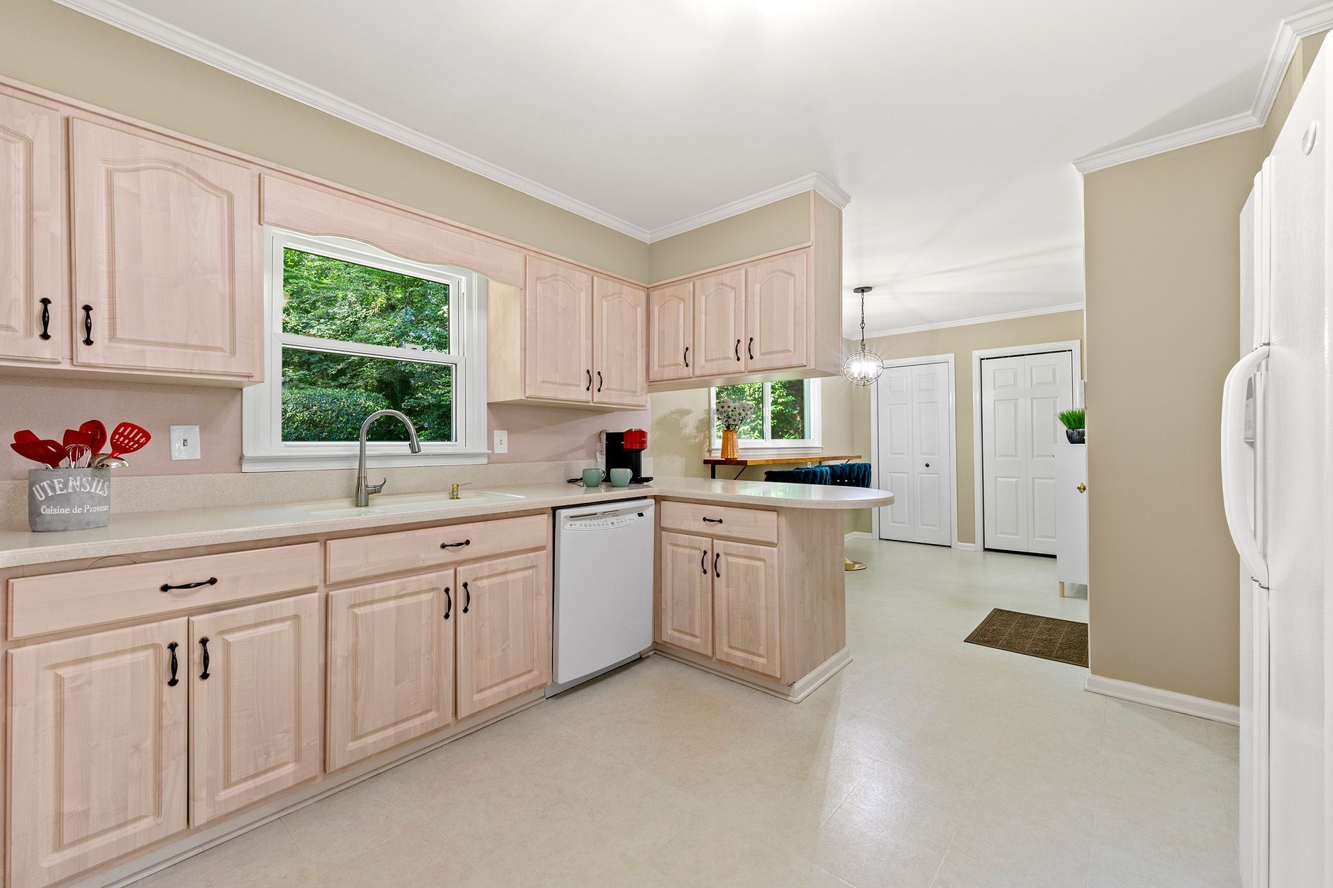 A kitchen with pink cabinets , white appliances , a sink , and a window.