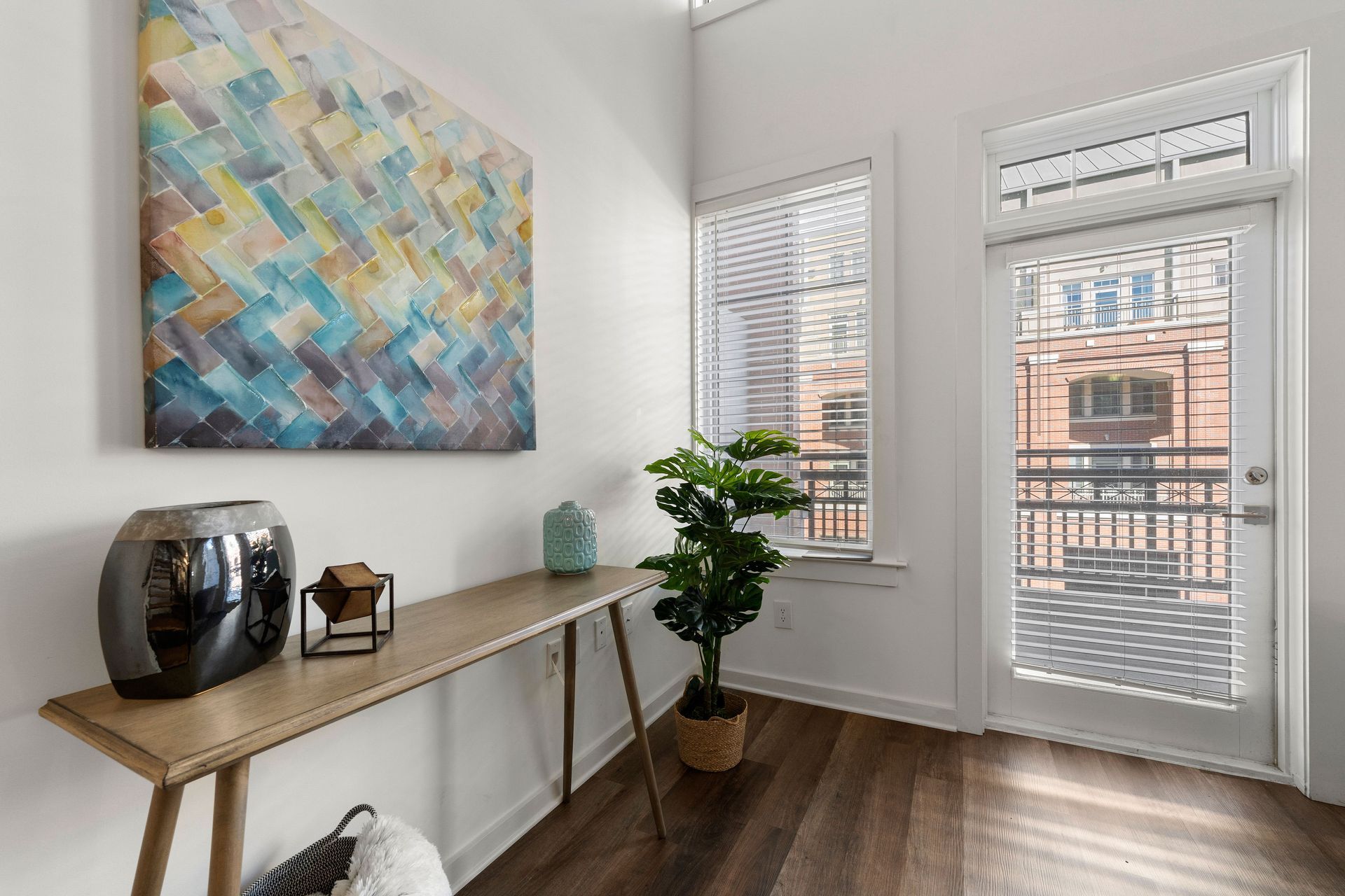 A living room with hardwood floors , a table , a painting on the wall and a sliding glass door.