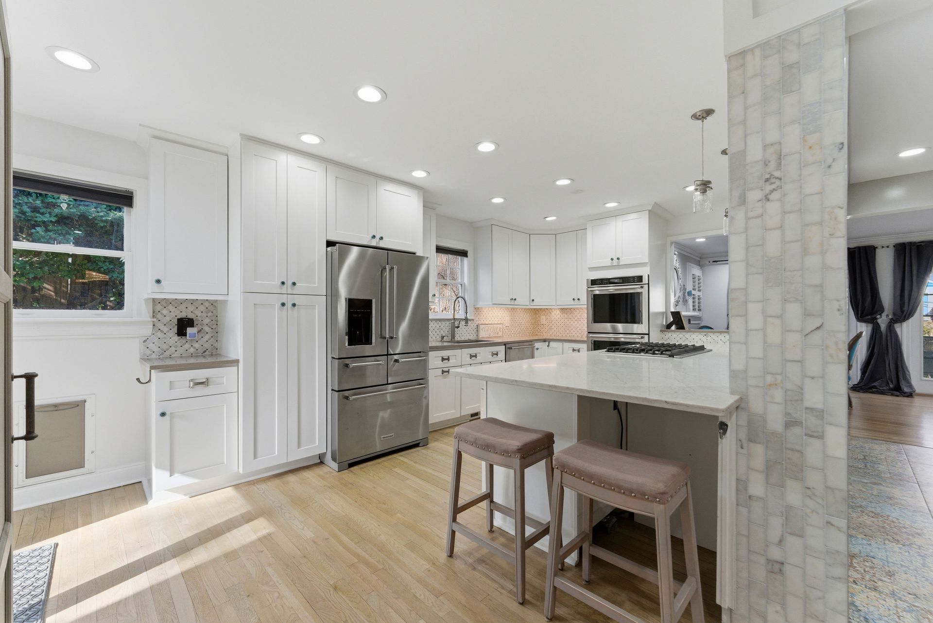 Bright, modern kitchen with white cabinets, stainless steel appliances, a center island with stools, and light wood floors.