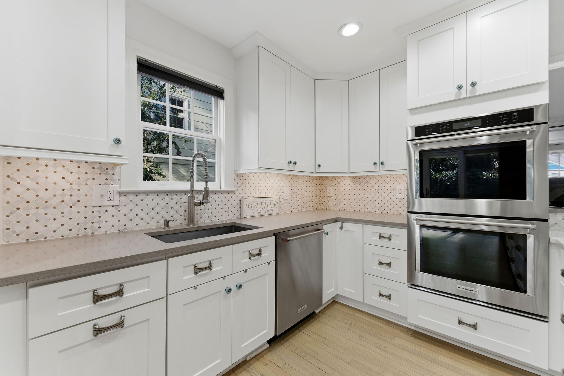 A modern, well-lit kitchen with white cabinetry, light countertops, stainless steel appliances, and a tiled backsplash.