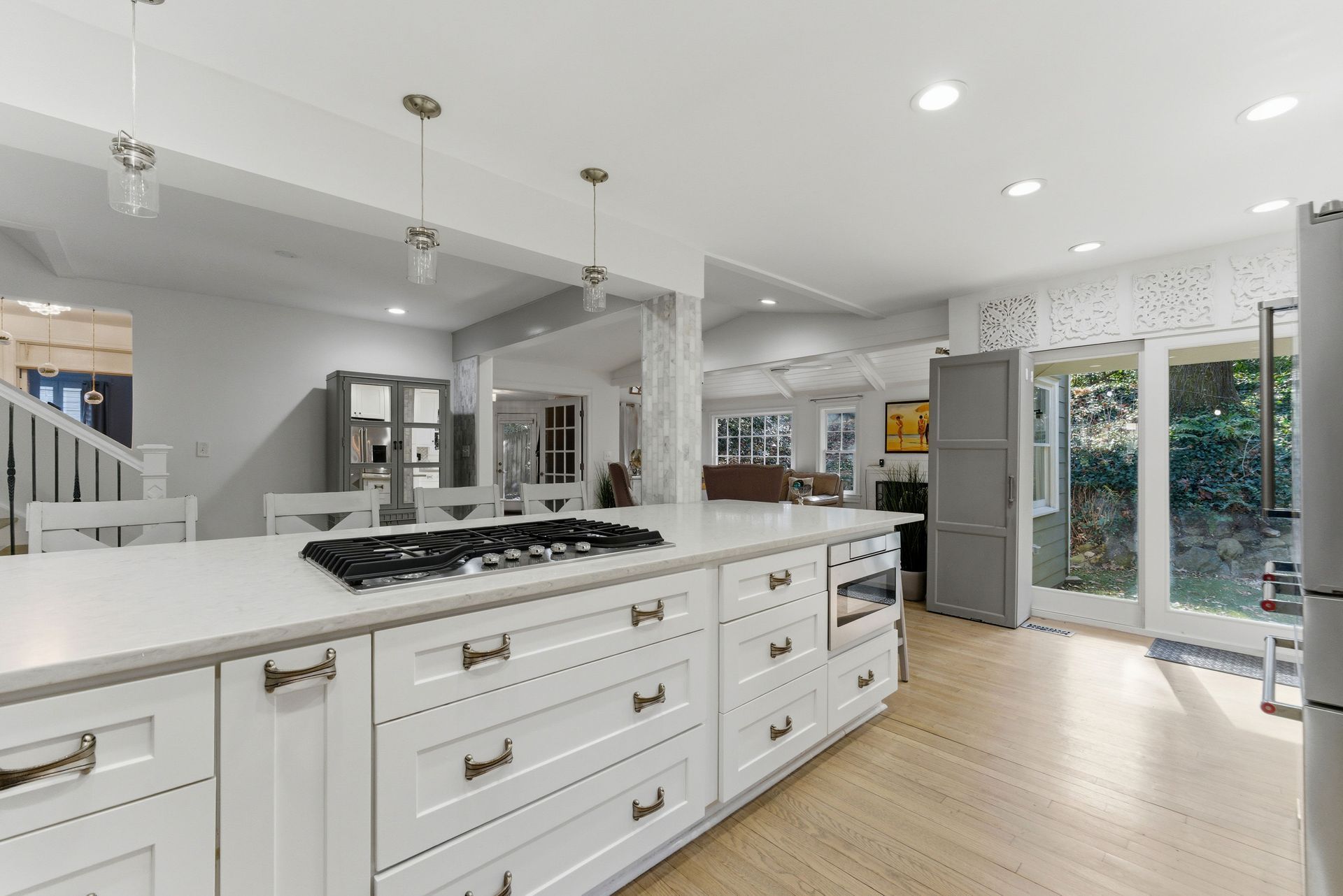 A modern, bright kitchen with white cabinets, a large island with a gas cooktop, and light wood flooring.