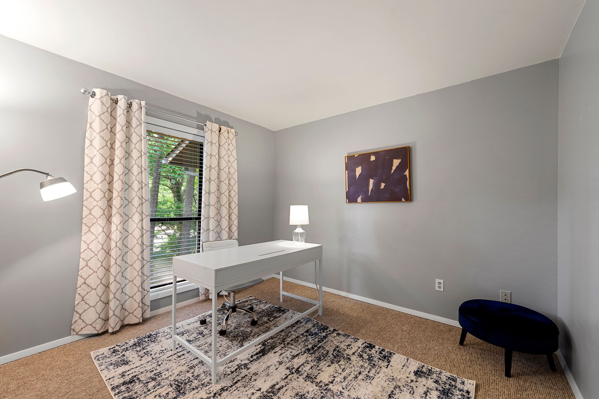 A room with a desk , chair , lamp and rug.