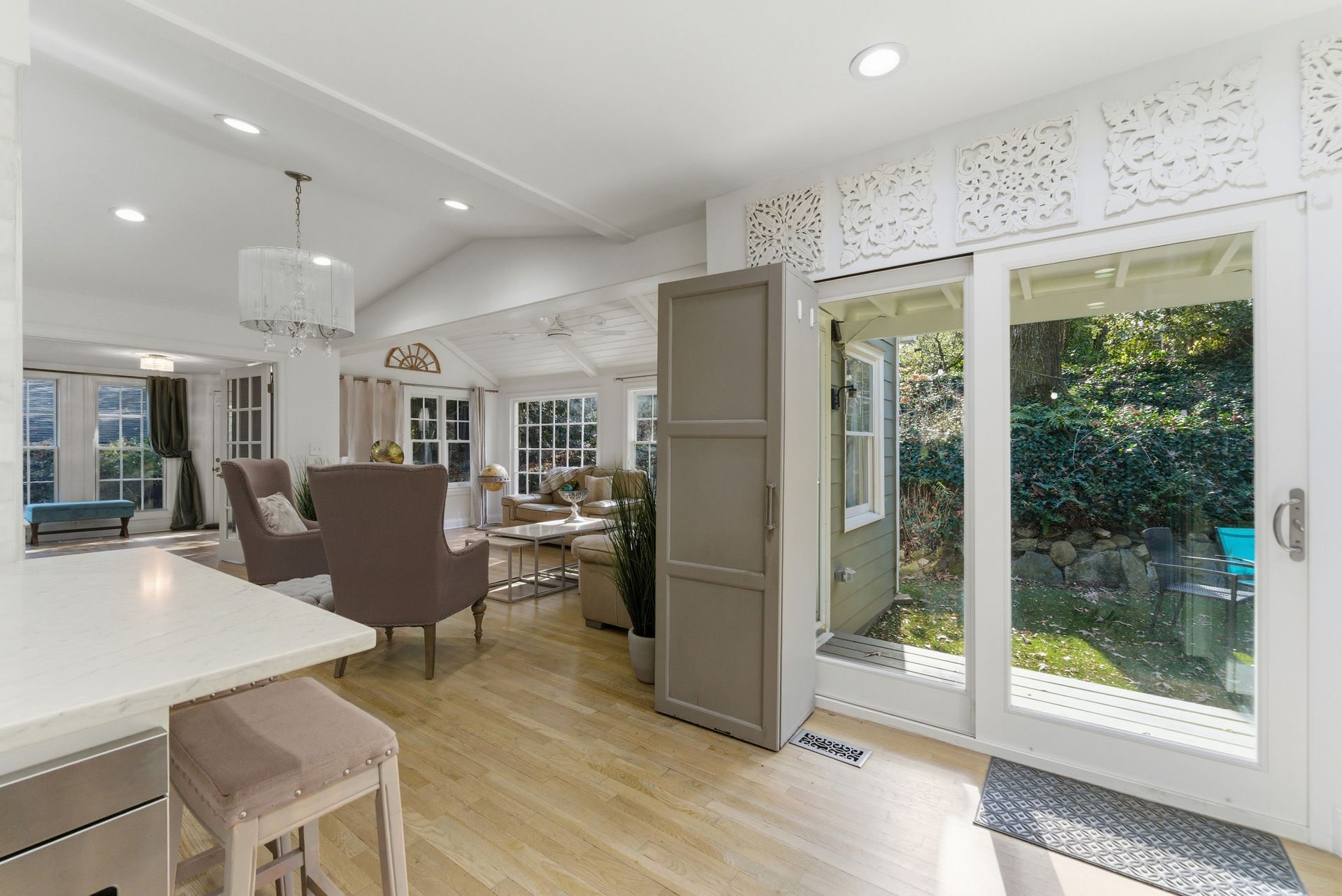 A modern, open-concept living area with light wood floors, a breakfast bar, and a view to an outdoor patio through doors.