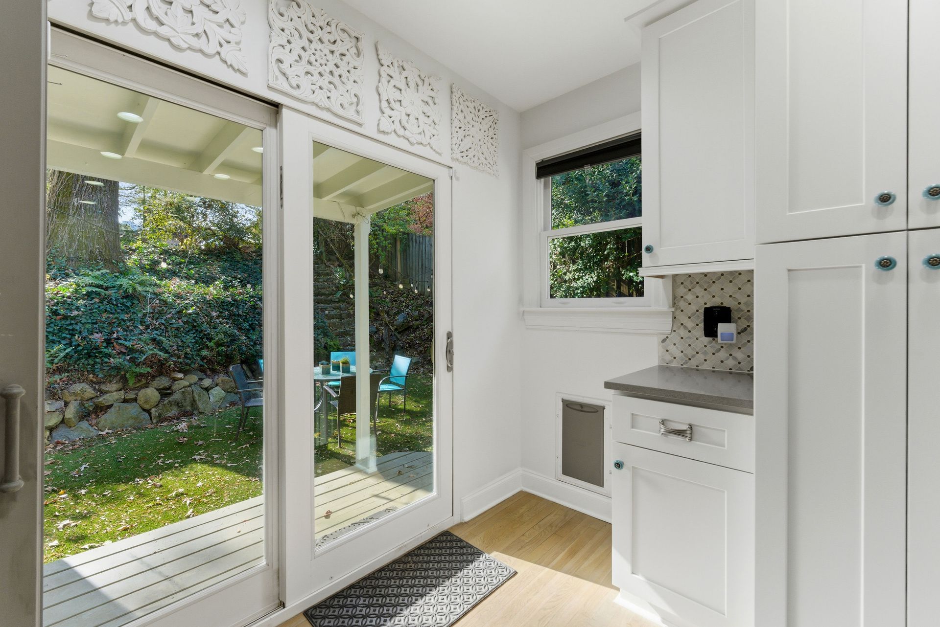 A brightly lit entryway with white cabinets and a sliding glass door opening to a backyard patio.