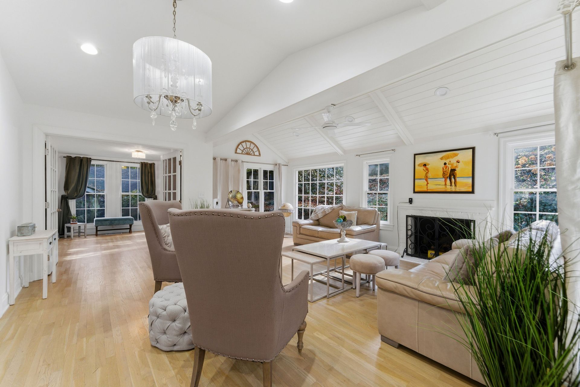 A brightly lit, spacious living room with hardwood floors, vaulted ceilings, neutral furniture, and a stone fireplace.