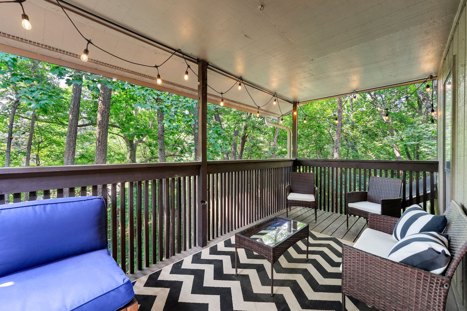 A porch with a blue couch , chairs , a coffee table and a rug.