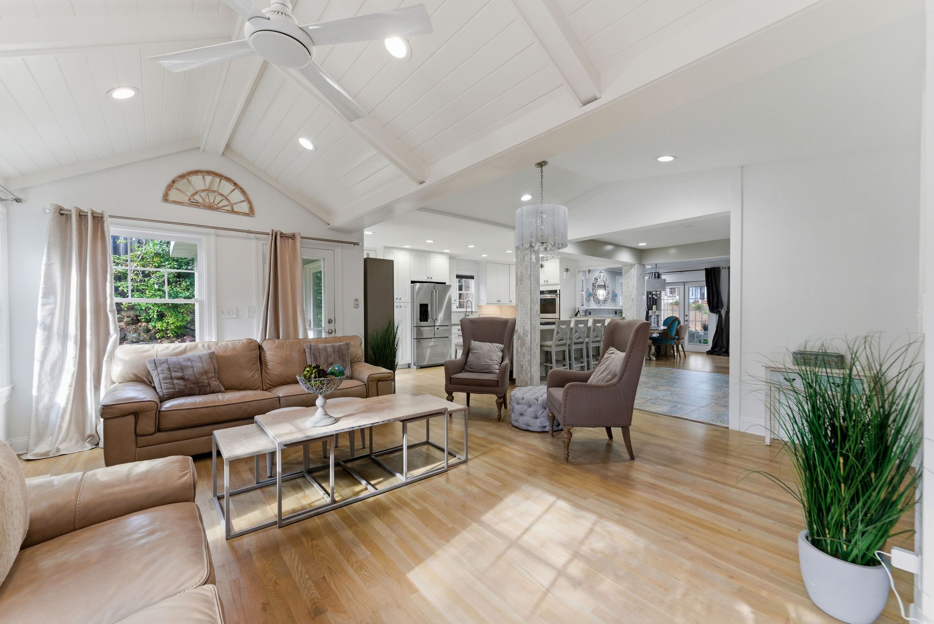 A bright, open-plan living room with vaulted ceilings, beige sofas, armchairs, and light wood floors.
