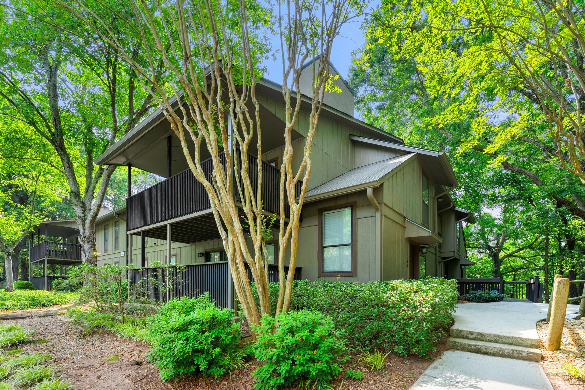 The house is surrounded by trees and bushes and has a balcony.