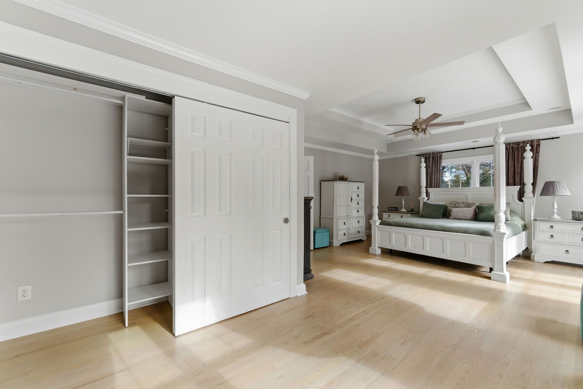 A bedroom with a four-poster white bed, white dresser, and a large closet with partially open sliding doors.