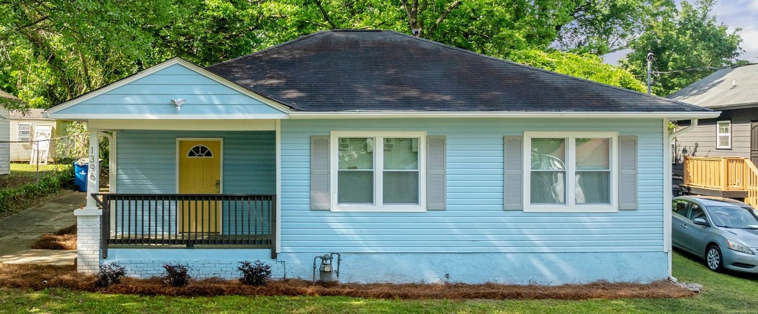 Light blue house with yellow door and gray shutters, sitting on a green lawn.