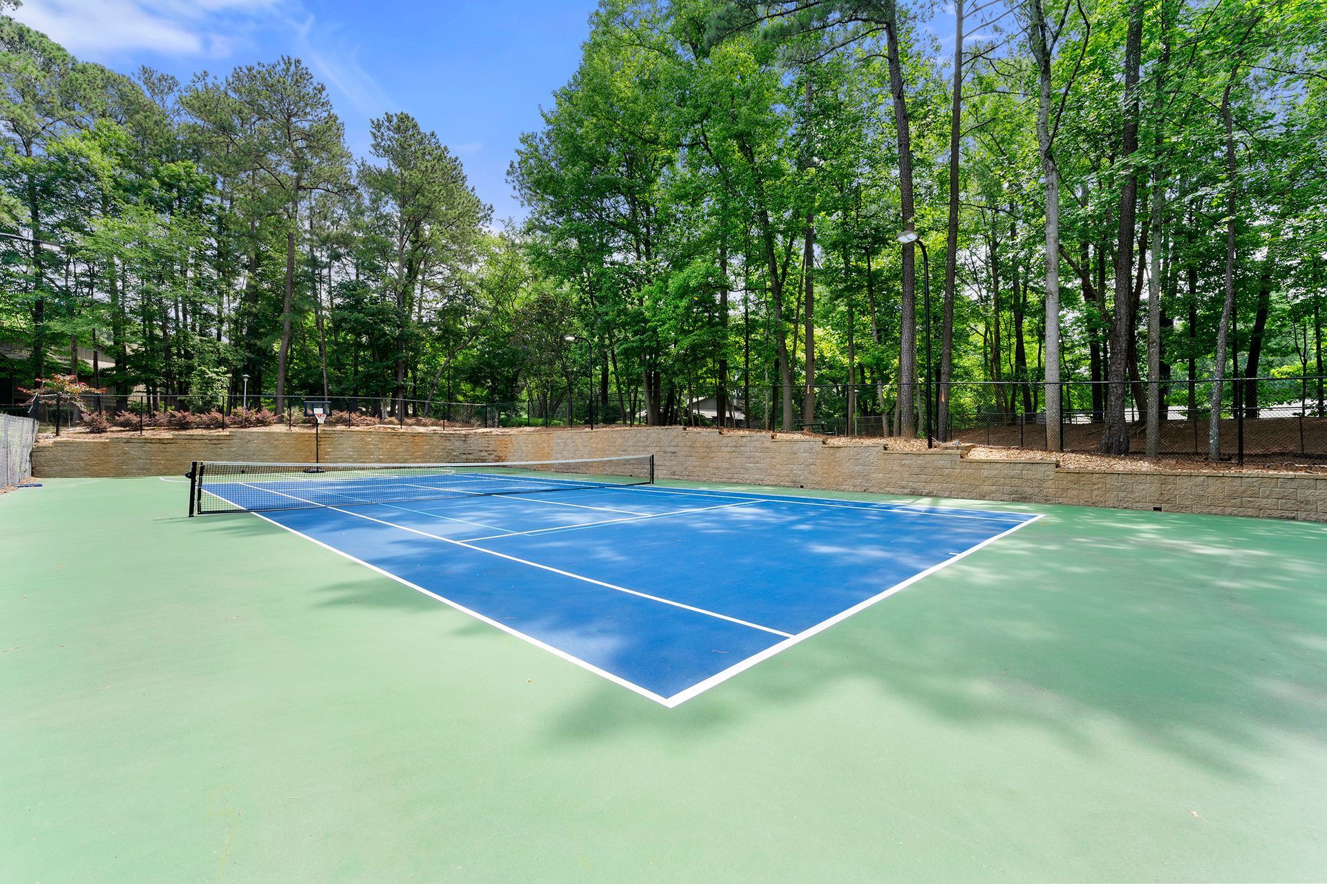 A tennis court surrounded by trees on a sunny day.