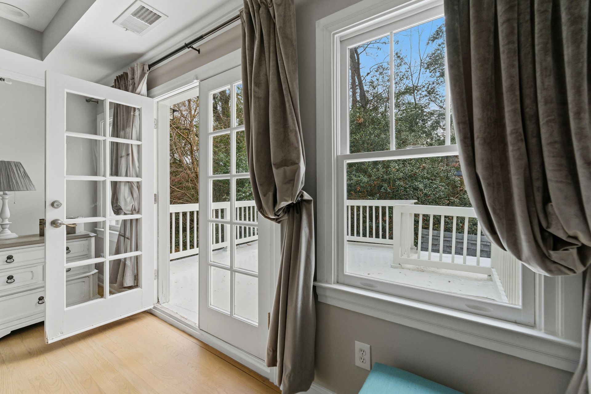 A bright room features white French doors and a window, both with taupe curtains, opening to a wooden deck.