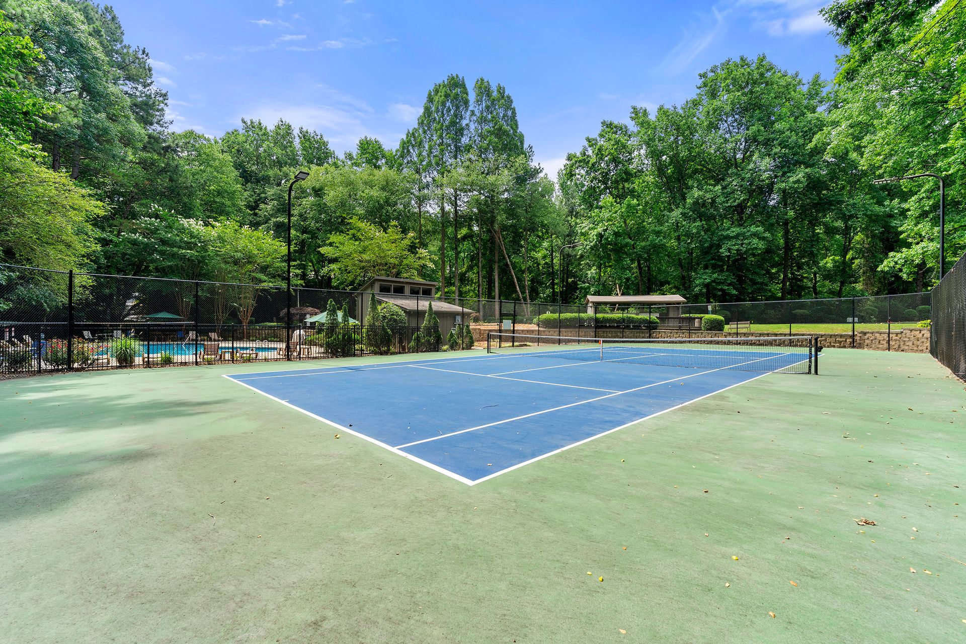A tennis court with trees in the background and a pool in the background