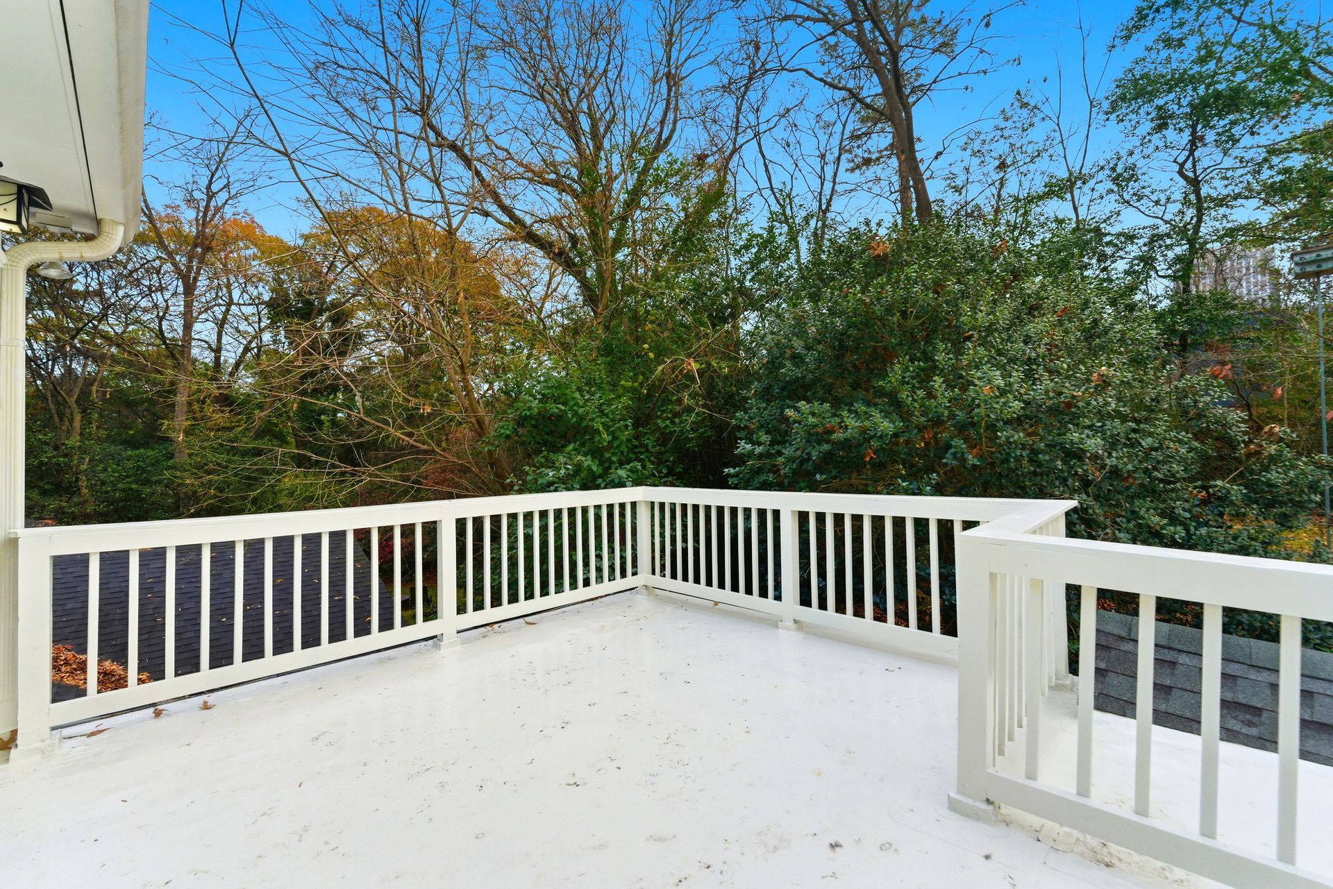 A white elevated deck with a matching railing, overlooking a background of lush green and autumn-colored trees.