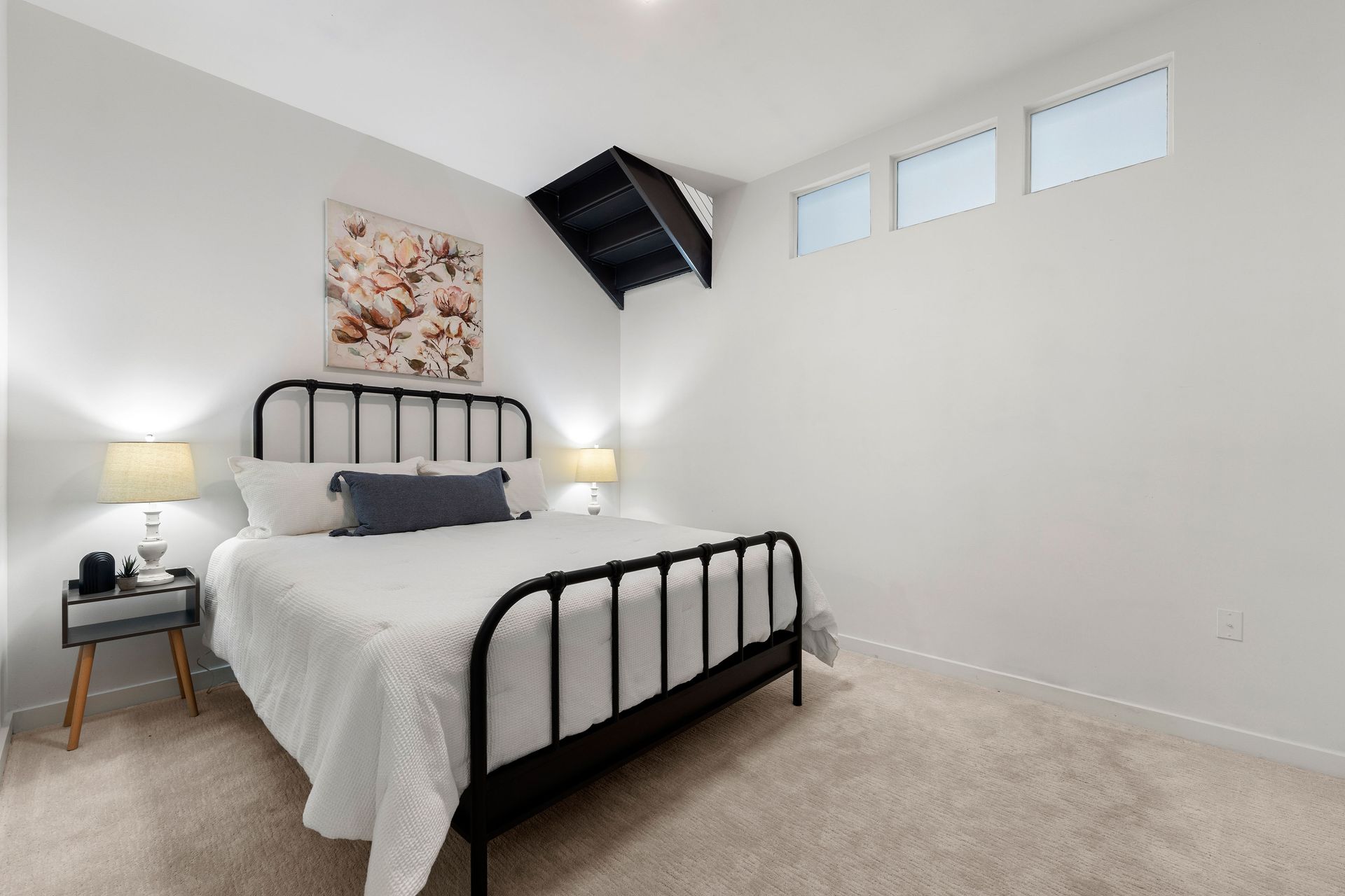 A bedroom with a bed , nightstand , lamps and a picture on the wall.