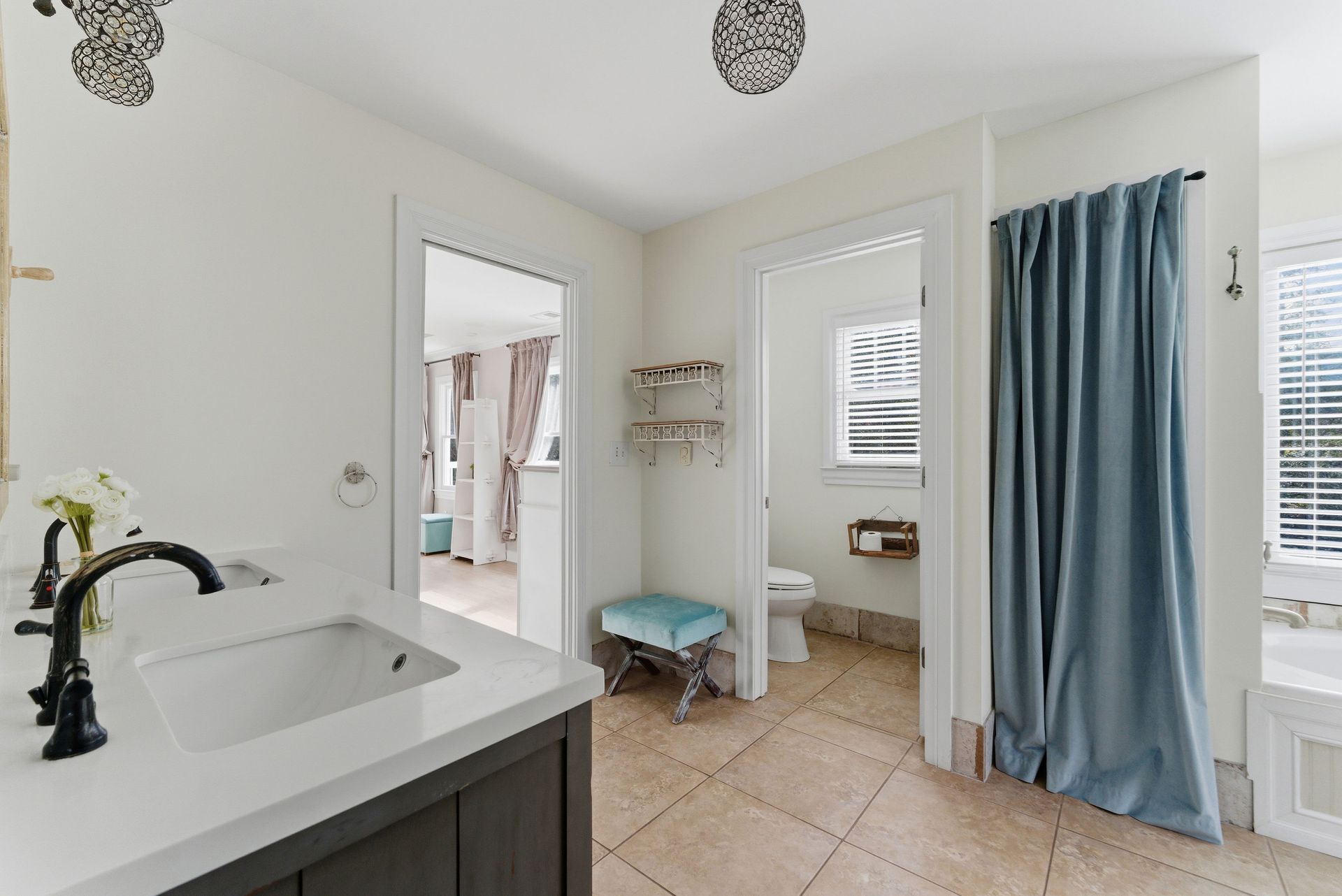 A bathroom interior featuring a white vanity with a dark faucet, a tiled floor, and an adjacent room with a blue curtain.