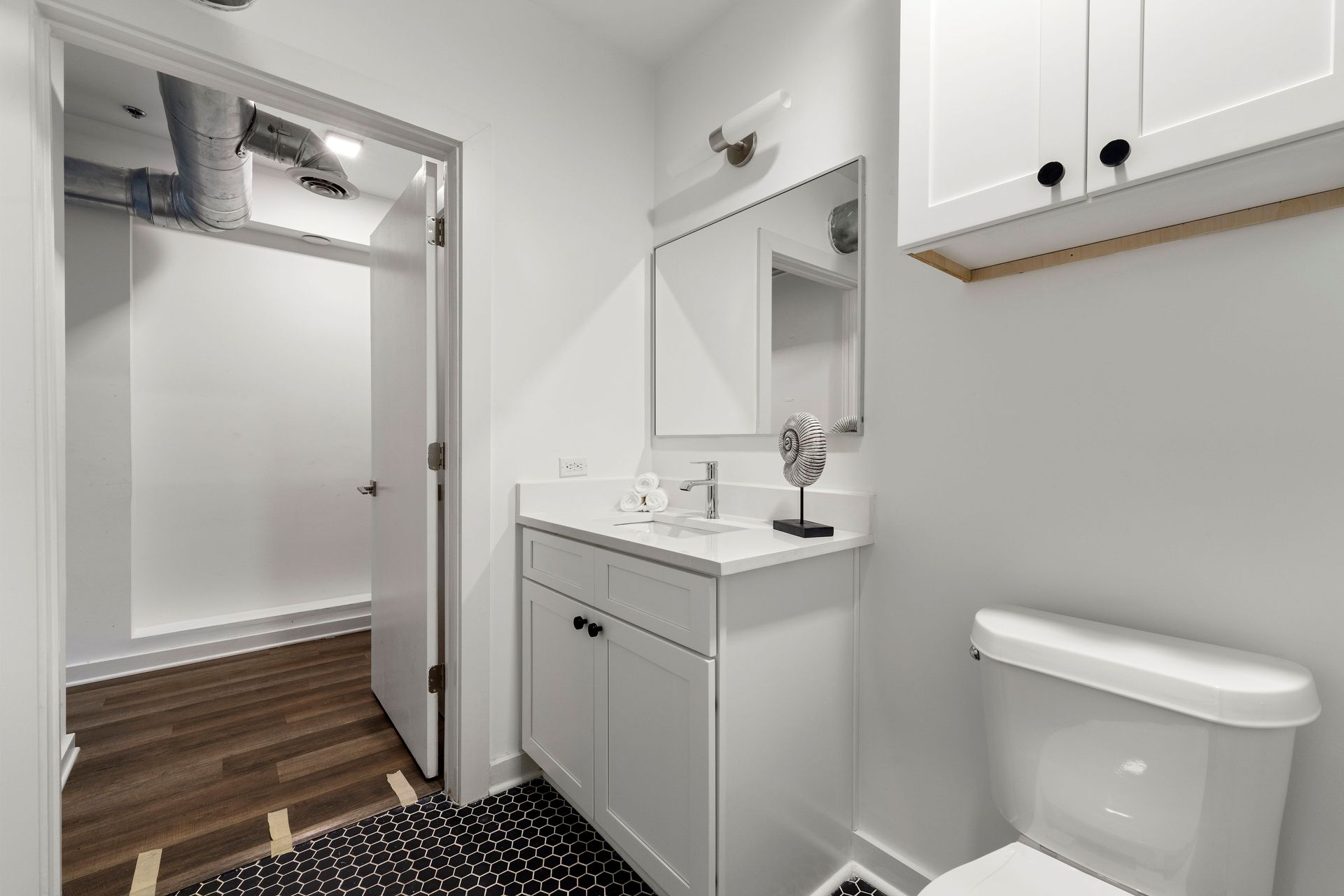 A bathroom with a toilet , sink , mirror and cabinets.
