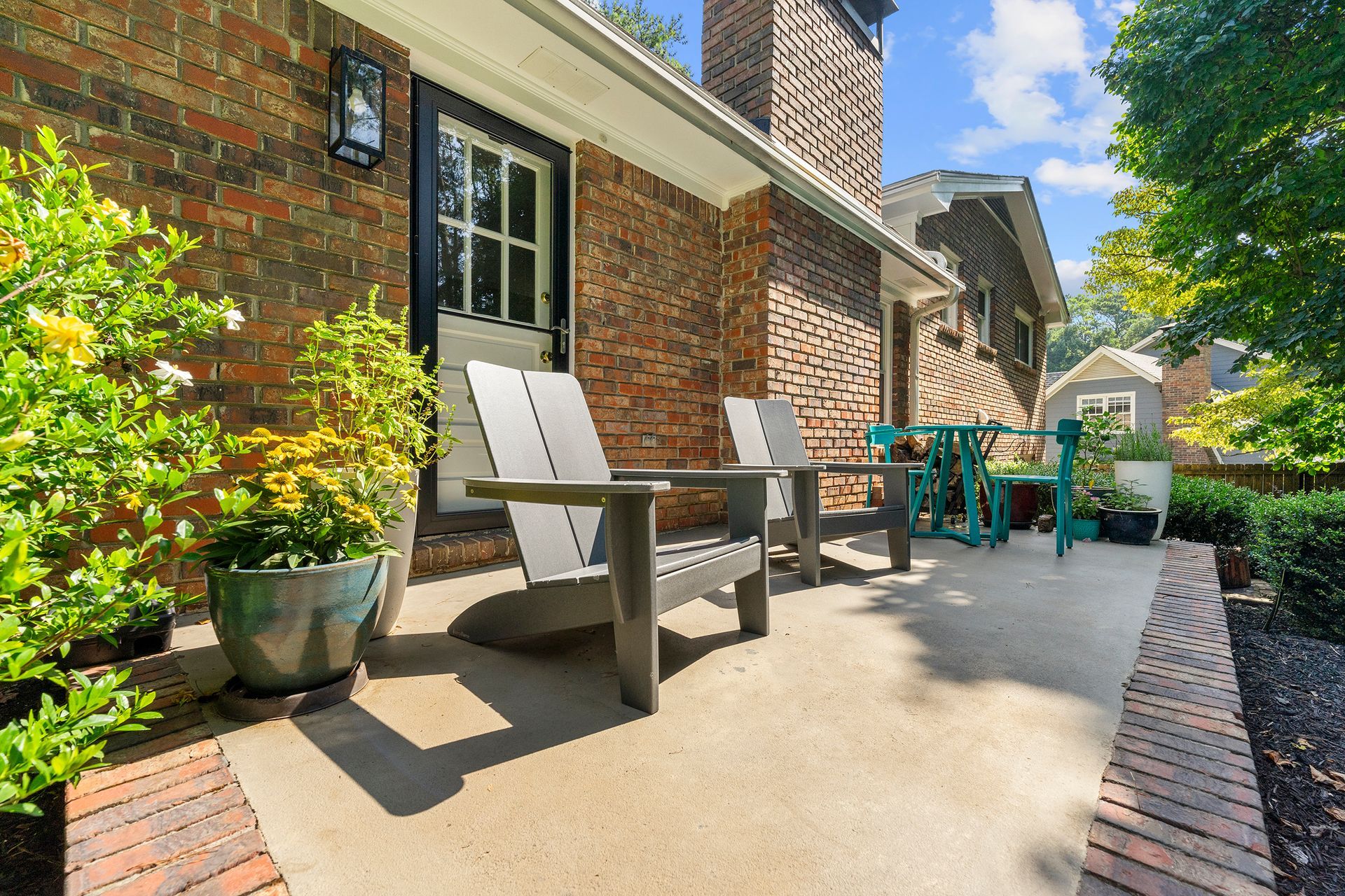 A patio with chairs and a table in front of a brick house.