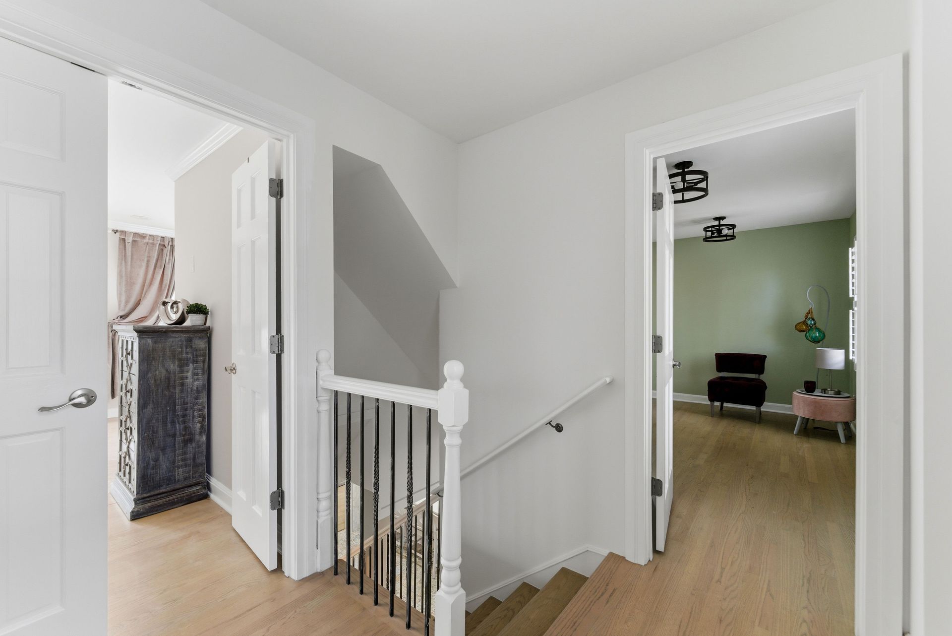 Hallway with a staircase, white walls, light wood flooring, and doorways opening into two separate rooms.