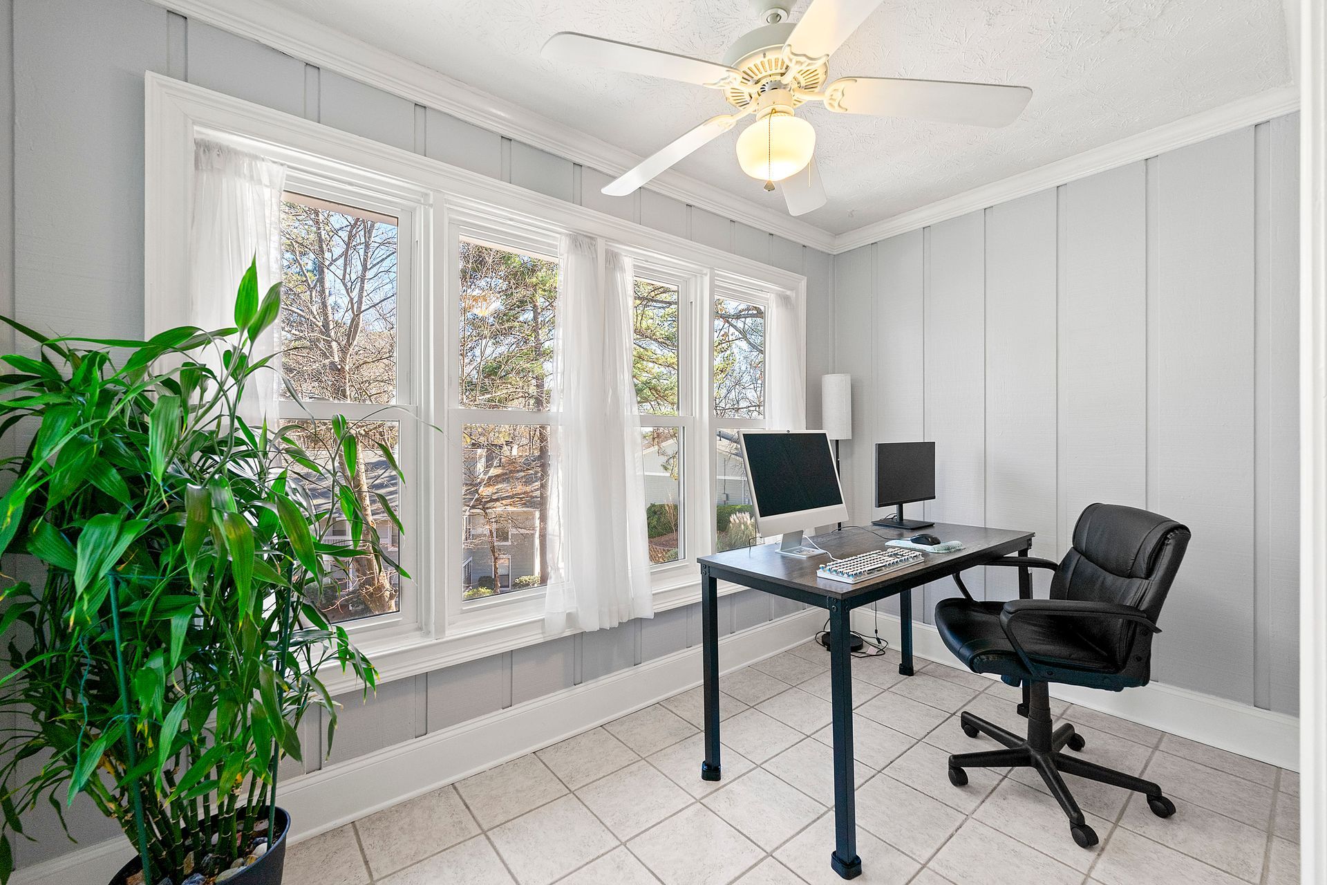 A home office with a desk , chair , computer and ceiling fan.