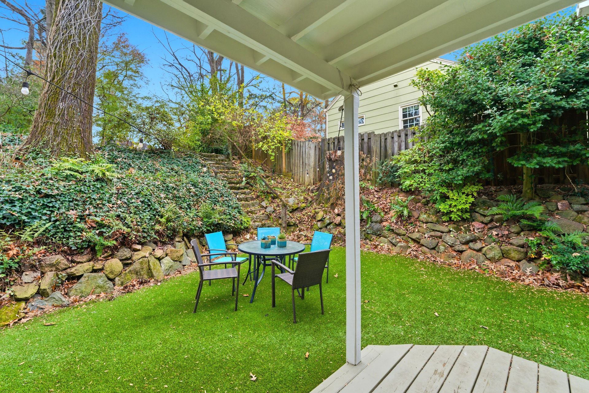 A small patio set with chairs and a table on a grassy backyard lawn seen from beneath a covered porch.