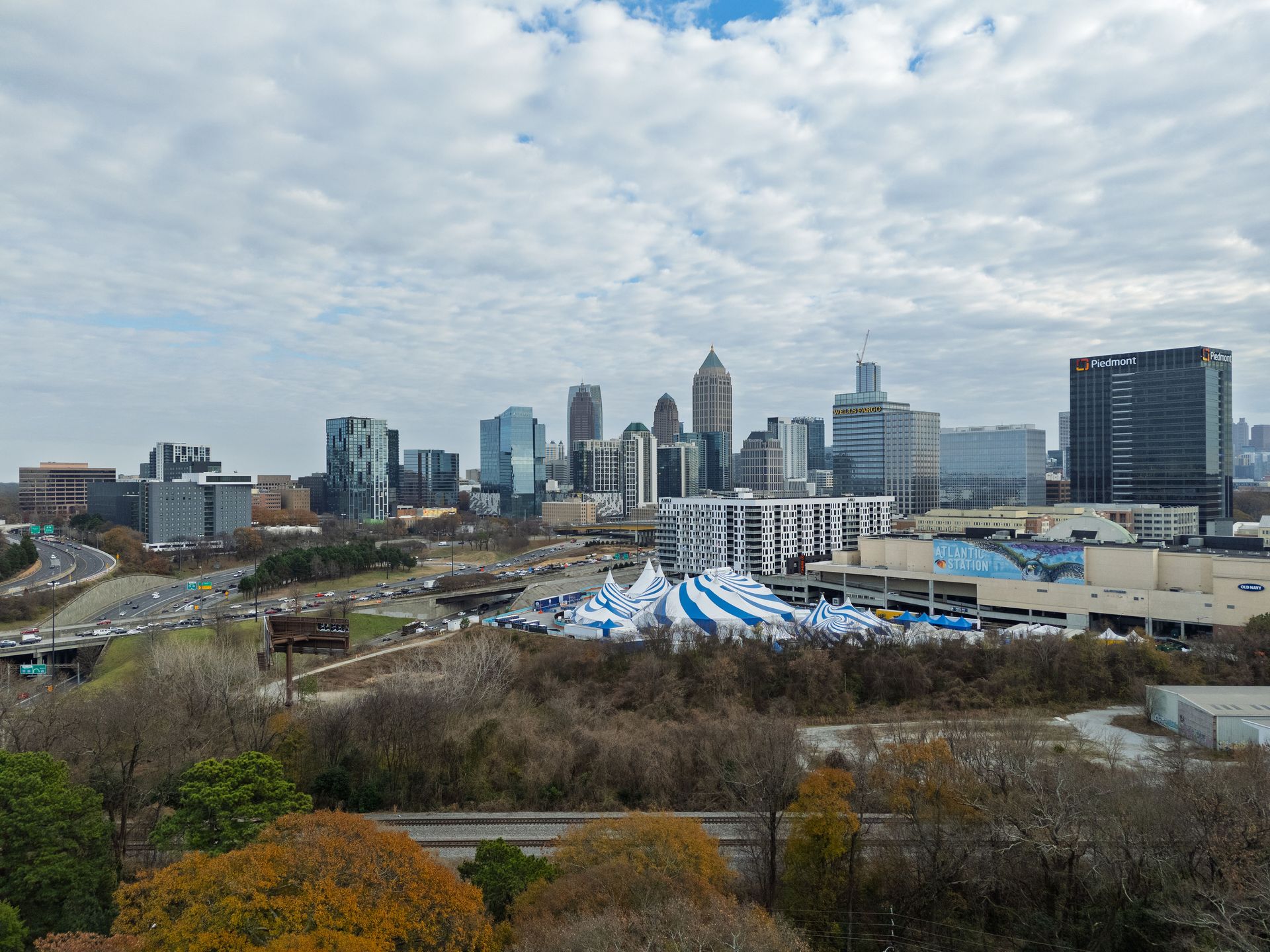 A cityscape of Atlanta, Georgia featuring downtown skyscrapers under a cloudy blue sky, with a tent setup in the foreground.