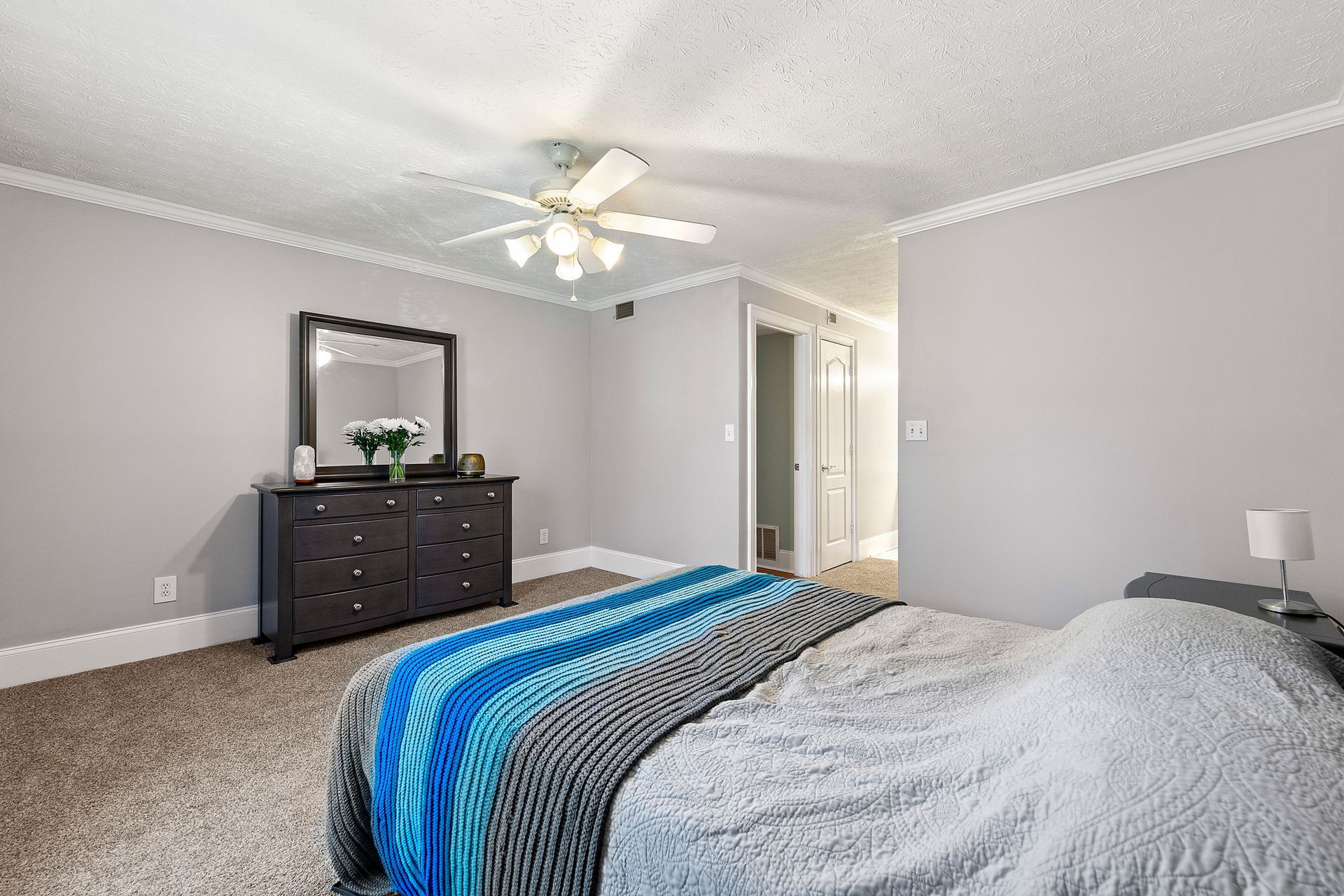 A bedroom with a bed , dresser , mirror and ceiling fan.